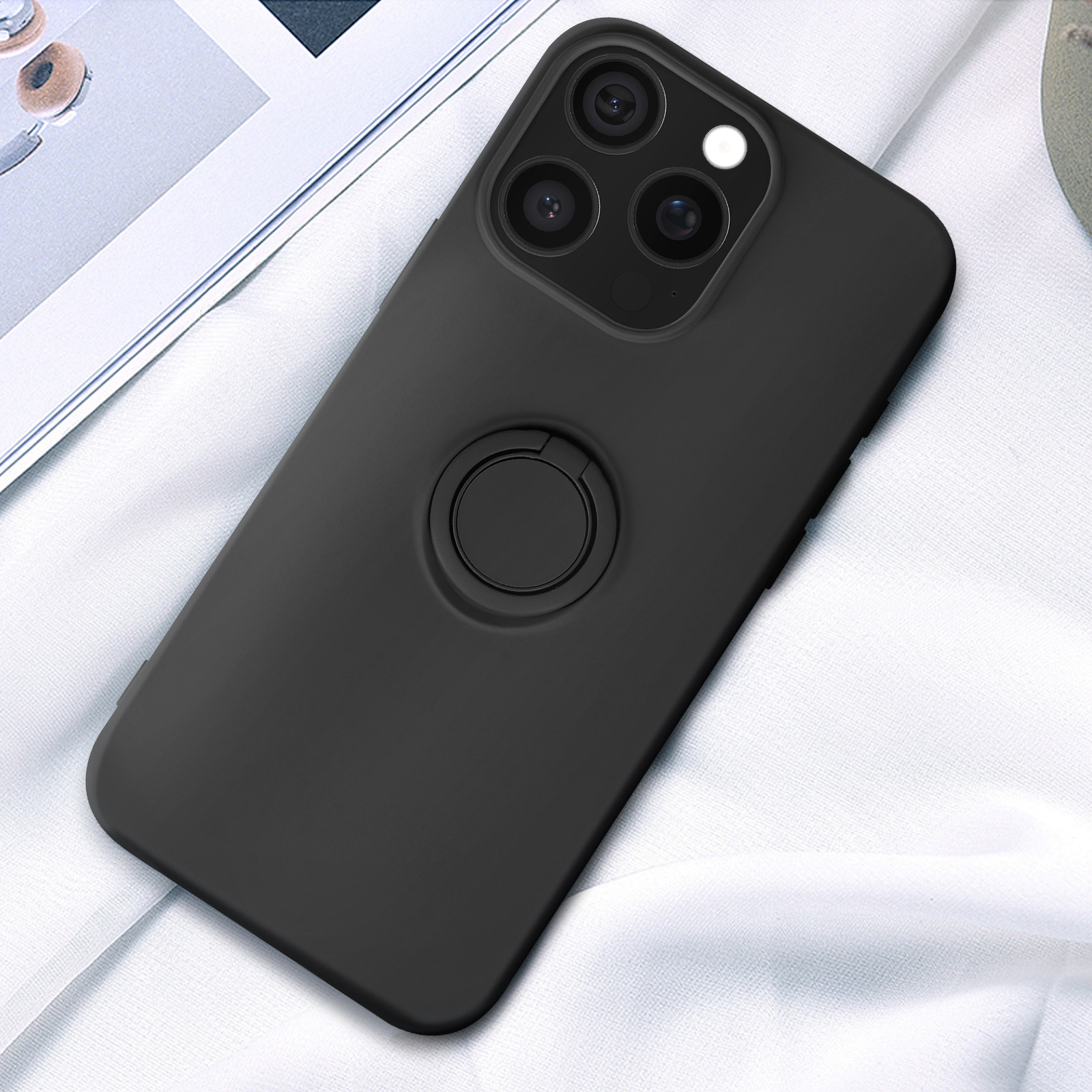 Custodia per telefono nera con anello su tessuto bianco. Il telefono ha un rialzo per la fotocamera.