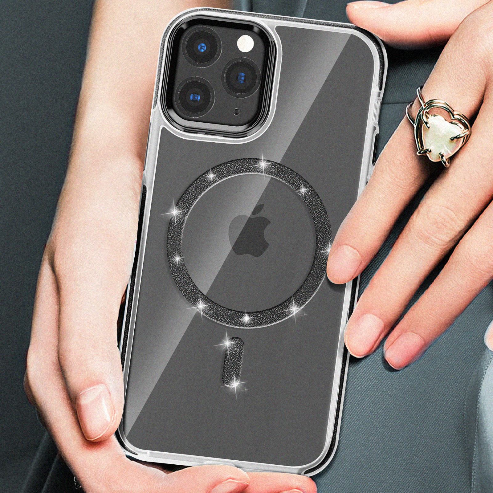 Mano che tiene un telefono con custodia trasparente, diamanti attorno alla fotocamera, un anello e logo Apple bianco.