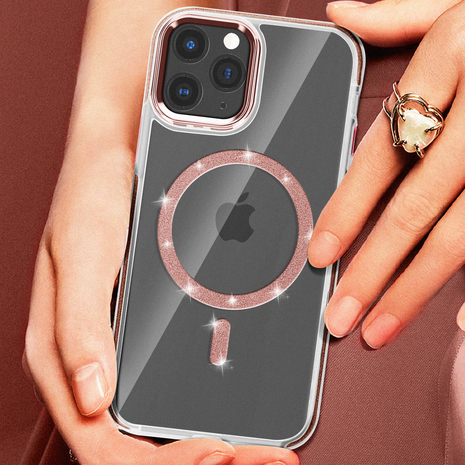 Custodia trasparente per iPhone con dettagli oro rosa. Mano che tiene il telefono con anello. Sfondo rosa.