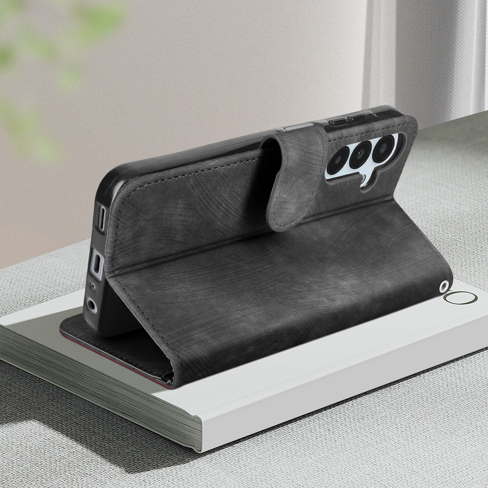 Custodia per telefono nera con un telefono all'interno, appoggiata su un libro. La custodia è strutturata.