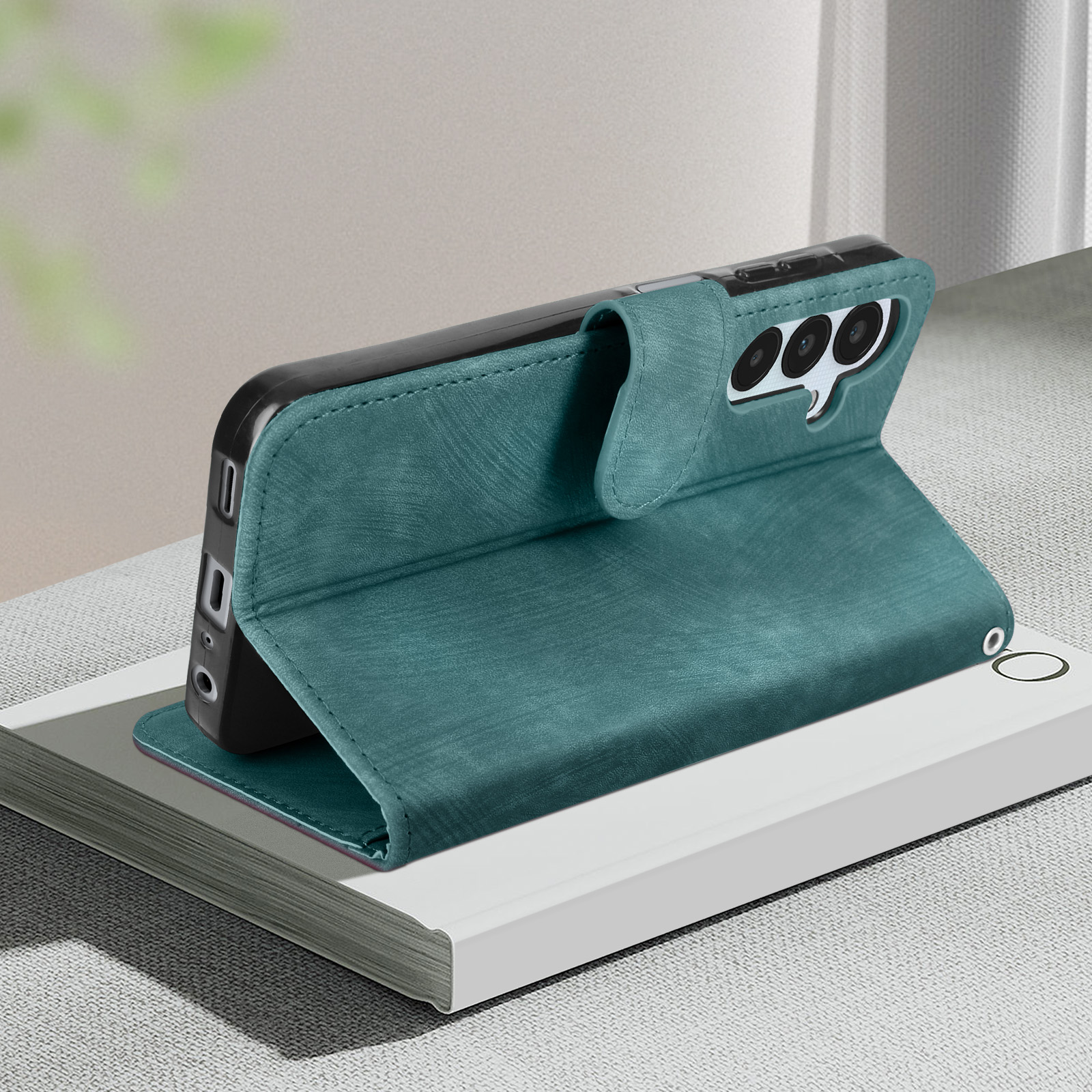 Custodia per telefono verde acqua, aperta, che mostra l'interno del telefono e gli slot per schede. Su un libro.