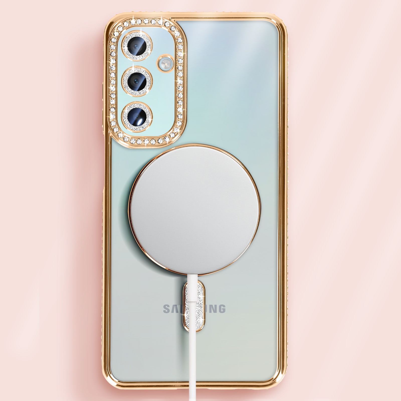 Custodia dorata con dettagli in cristallo, un pad di ricarica bianco e un telefono. Sfondo rosa.