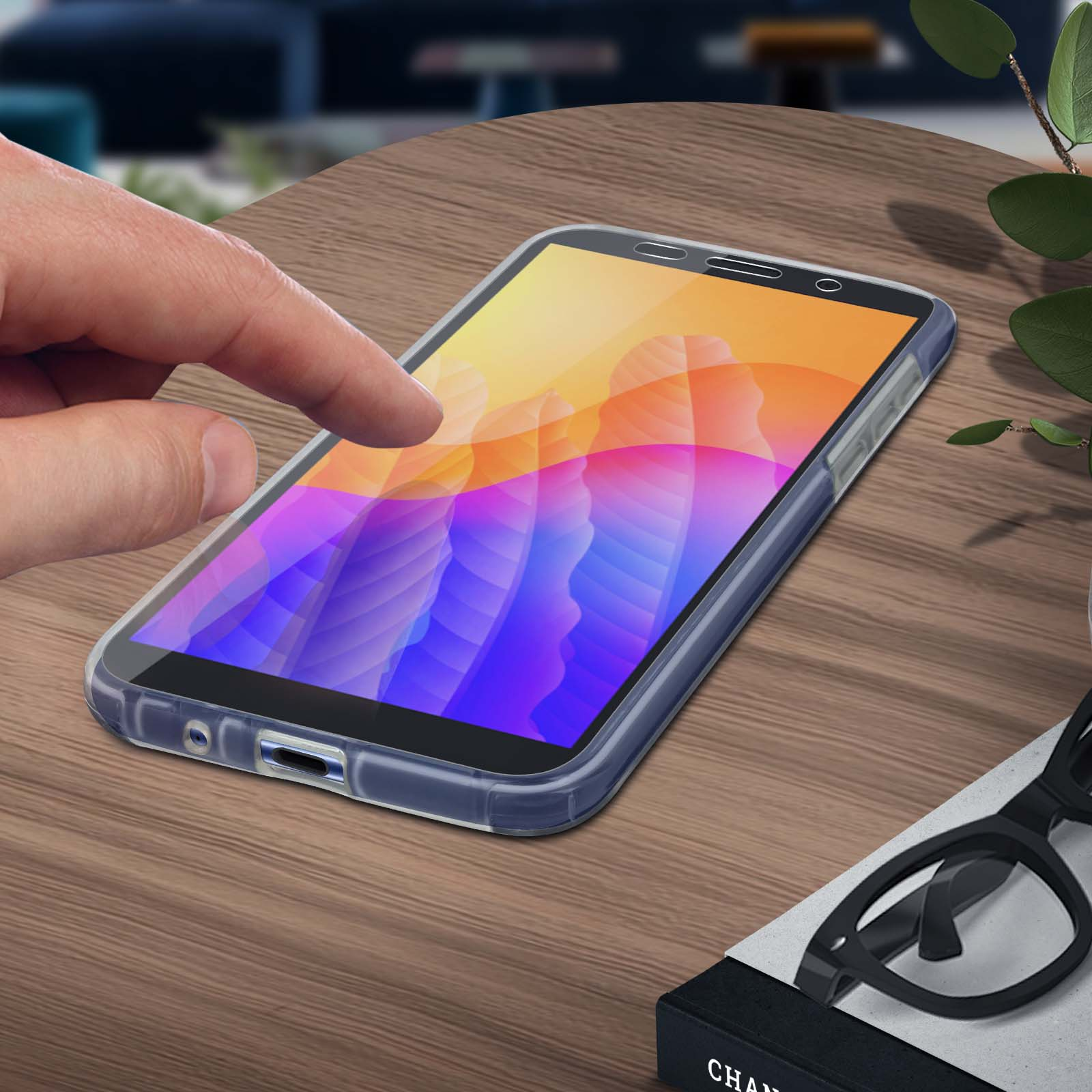 Een hand raakt een telefoon aan. De telefoon ligt op een houten tafel. Een bril en een boek liggen in de buurt.