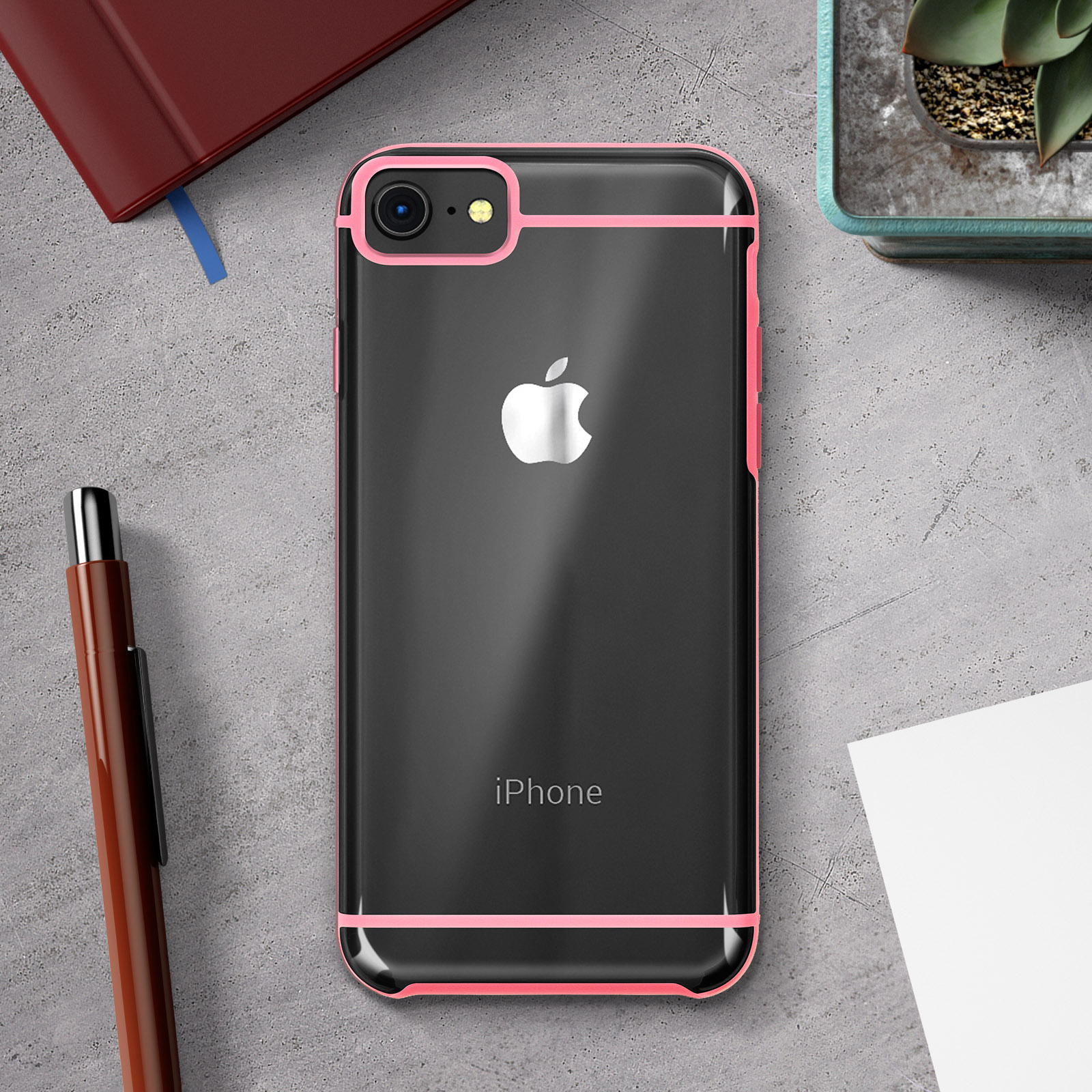 iPhone in custodia con bordi rosa. Penna, blocco note e pianta su superficie grigia.