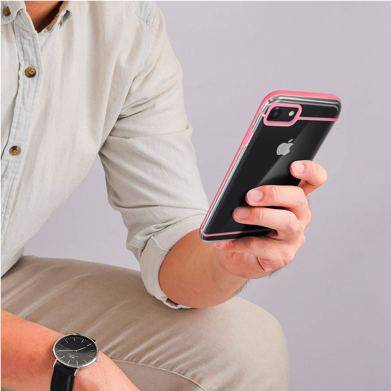 Persona che tiene un iPhone con custodia bordata di rosa. Orologio al polso, sfondo grigio.