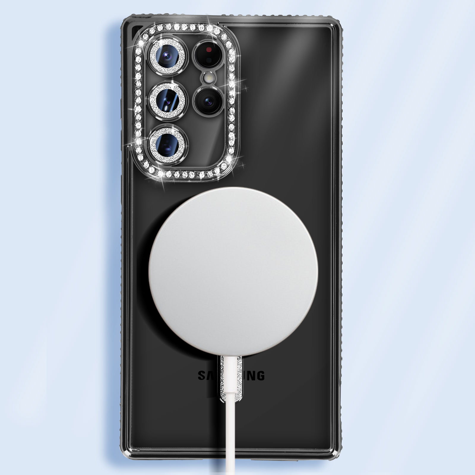 Schwarzes Telefon mit durchsichtiger Hülle und Strasssteinen um die Kamera. Ein weißes magnetisches Ladepad ist befestigt.
