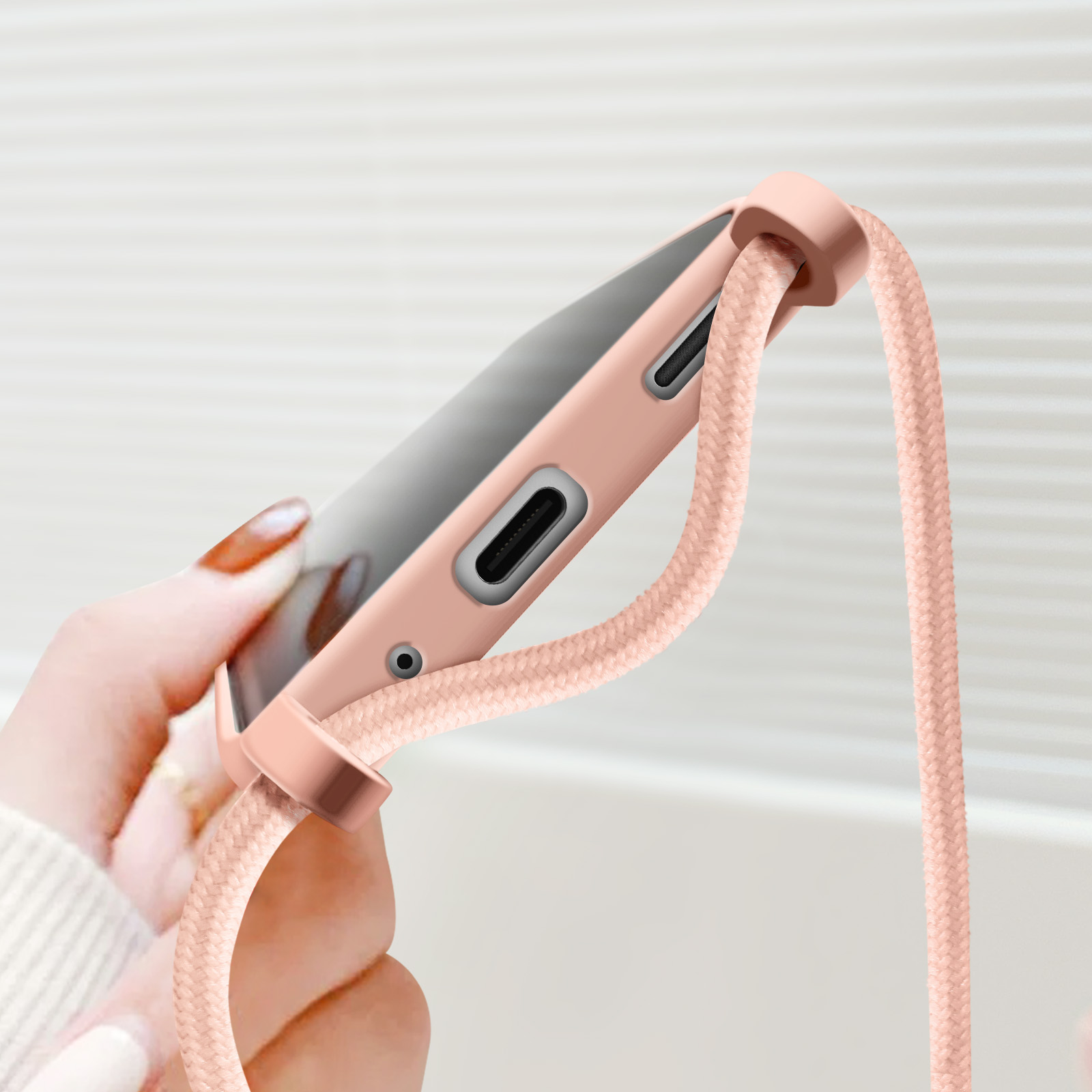 Una mano tiene una custodia per telefono con un cinturino rosa. La custodia è rosa e il cinturino è in tinta.