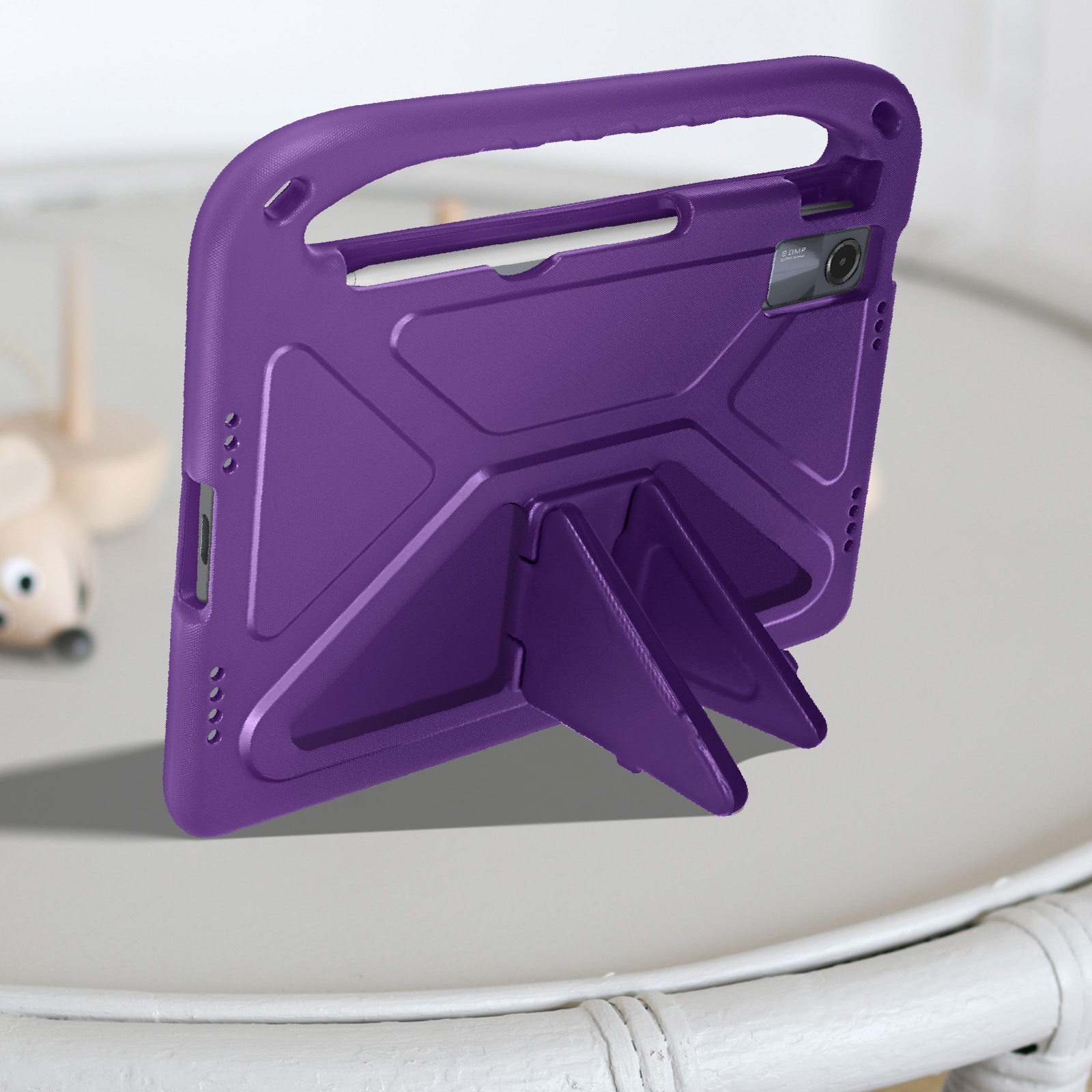 Una custodia viola per tablet è appoggiata con un cavalletto su un tavolo bianco vicino a un giocattolo.