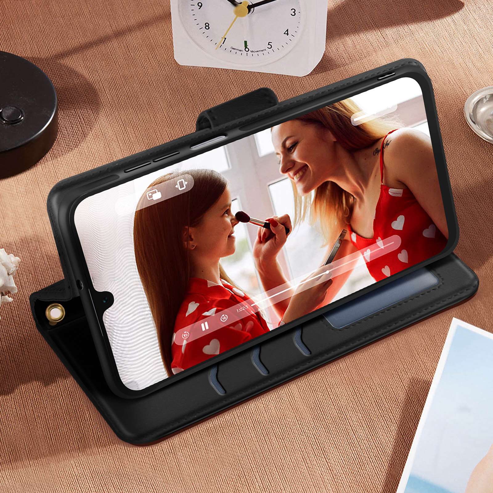 Funda de teléfono negra con teléfono dentro. Muestra una videollamada con una mujer maquillándose.