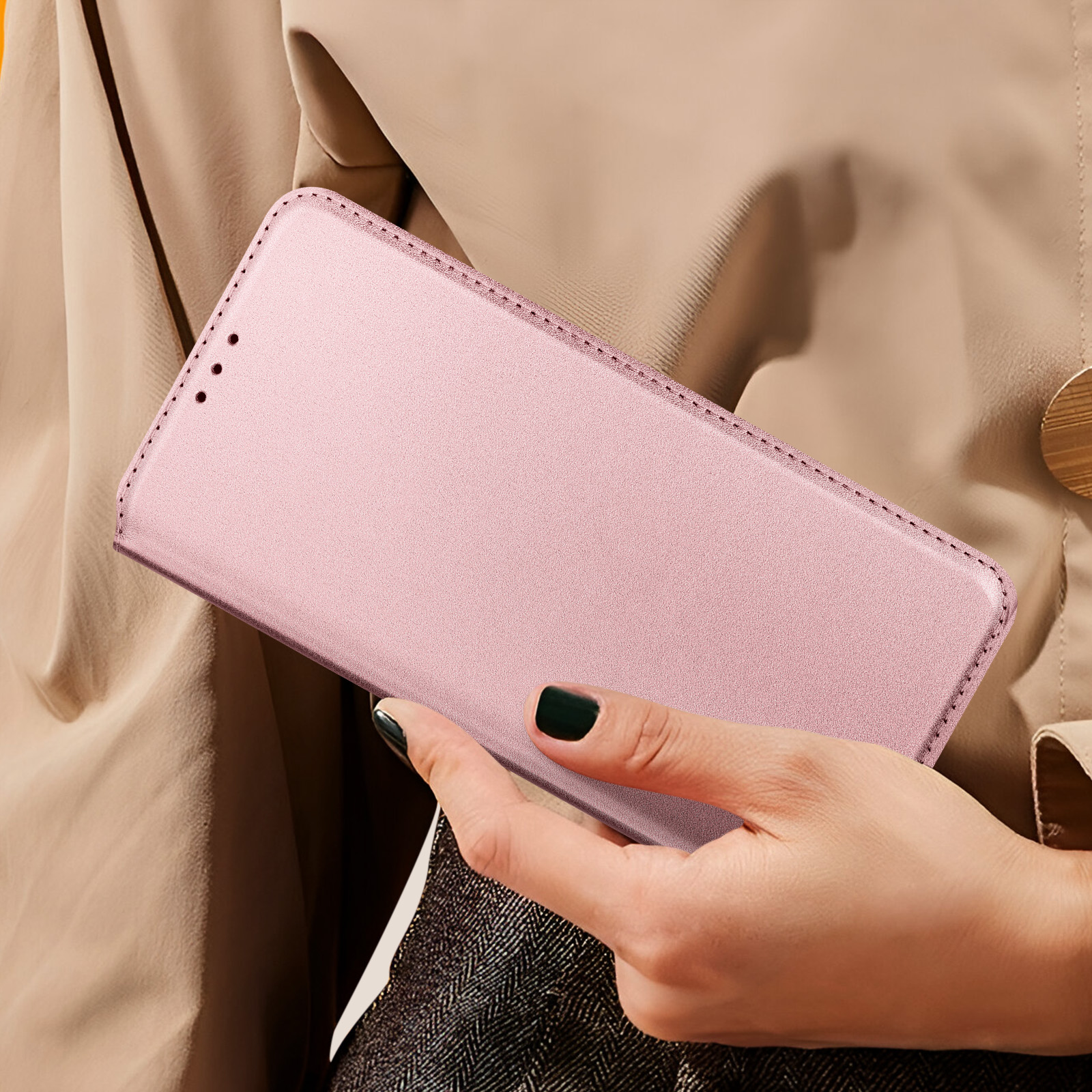 Mano che tiene una custodia rosa per telefono. Unghie nere. Sfondo di abbigliamento beige.