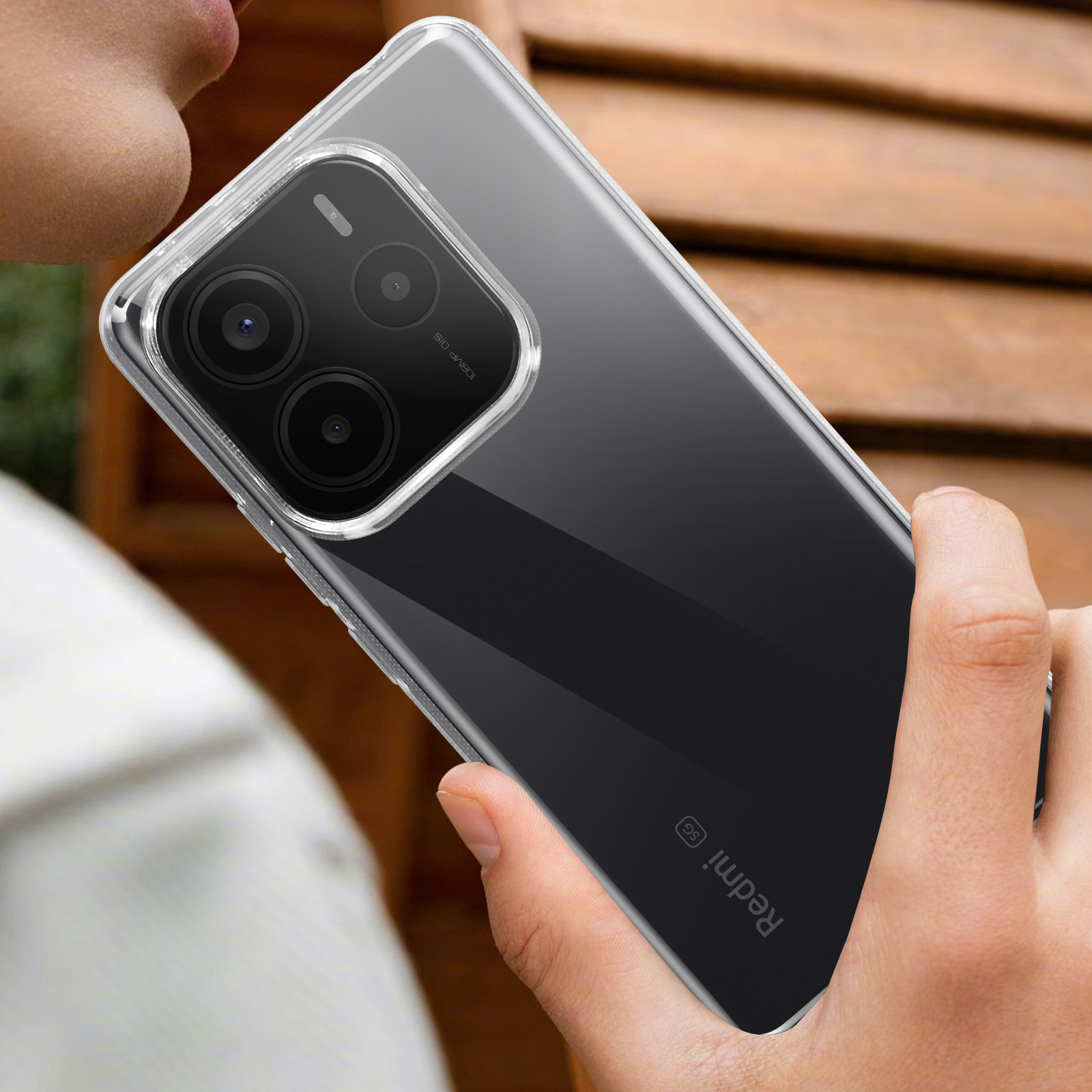 Custodia trasparente su una mano, copre parzialmente il retro del telefono con lenti della fotocamera e logo Redmi.
