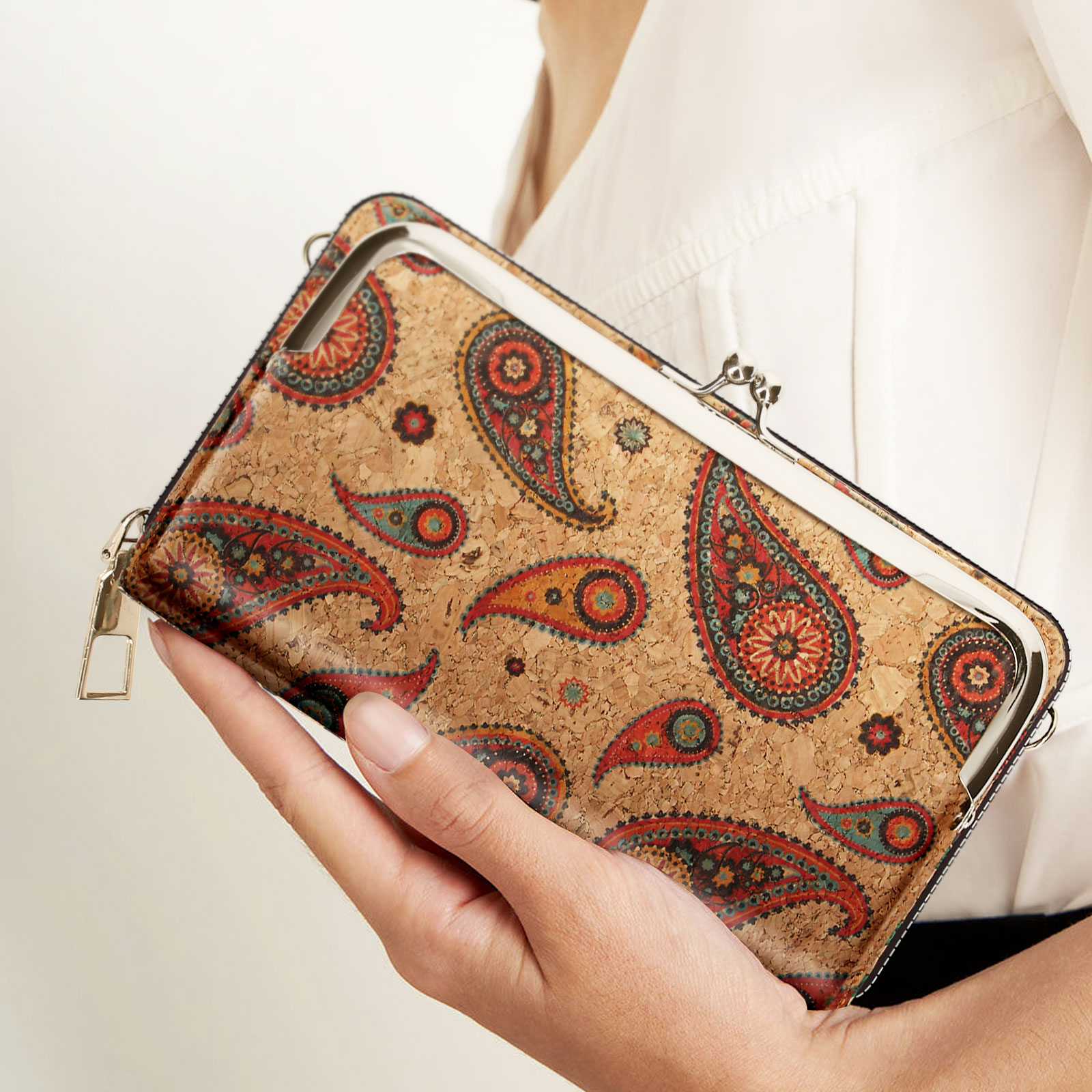 Die Hand einer Frau hält eine Geldbörse mit Paisley-Muster.