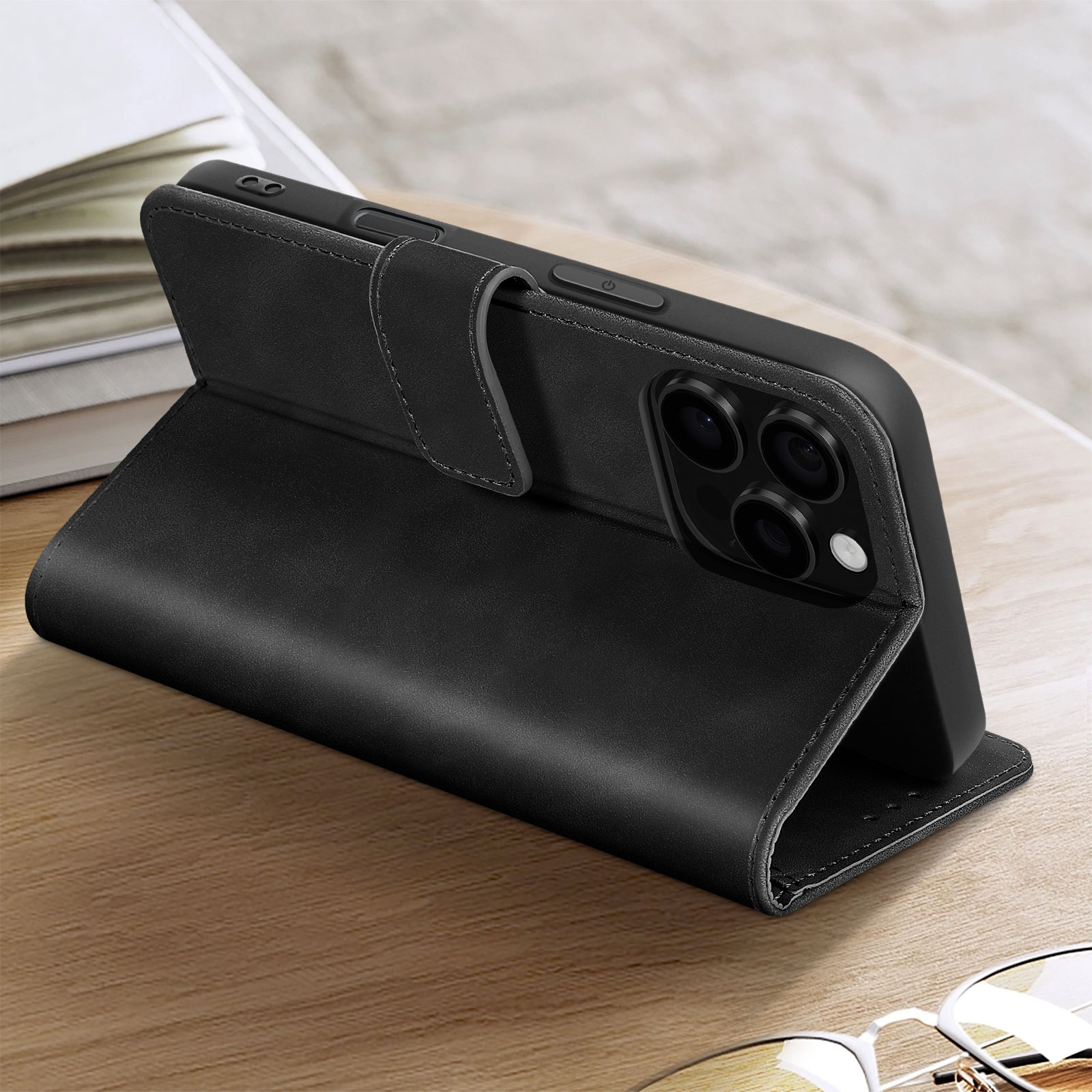 Custodia nera per telefono aperta su un tavolo di legno. Un libro sullo sfondo sfocato.
