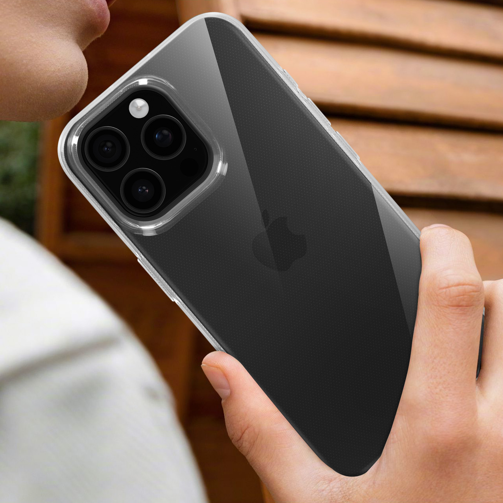 Un telefono con tre fotocamere in una custodia trasparente, tenuto da una persona. Sfondo in legno leggermente sfocato.
