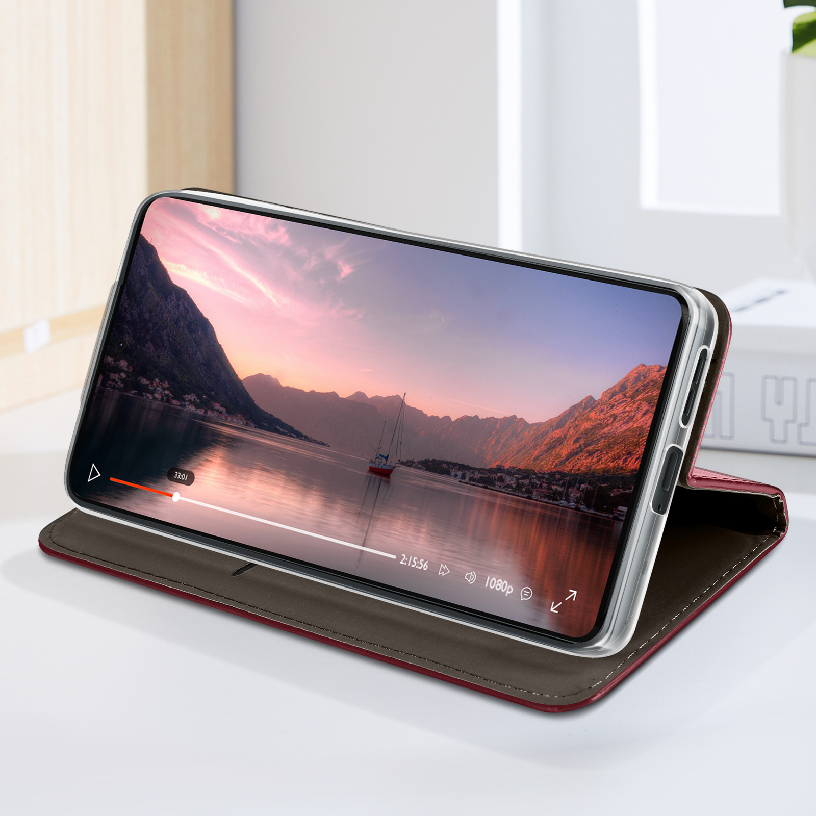 Telefono in una custodia in pelle rossa. Lo schermo mostra la riproduzione video. Barca sull'acqua.