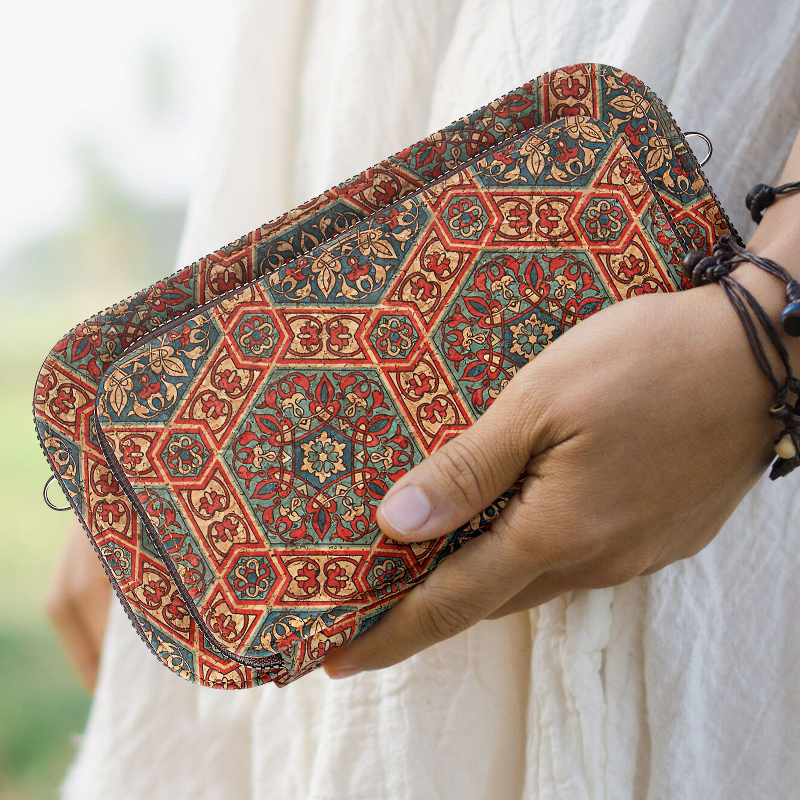 Hand hält eine Tasche mit buntem Muster. Die Tasche hat einen Reißverschluss. Hintergrund ist unscharf.