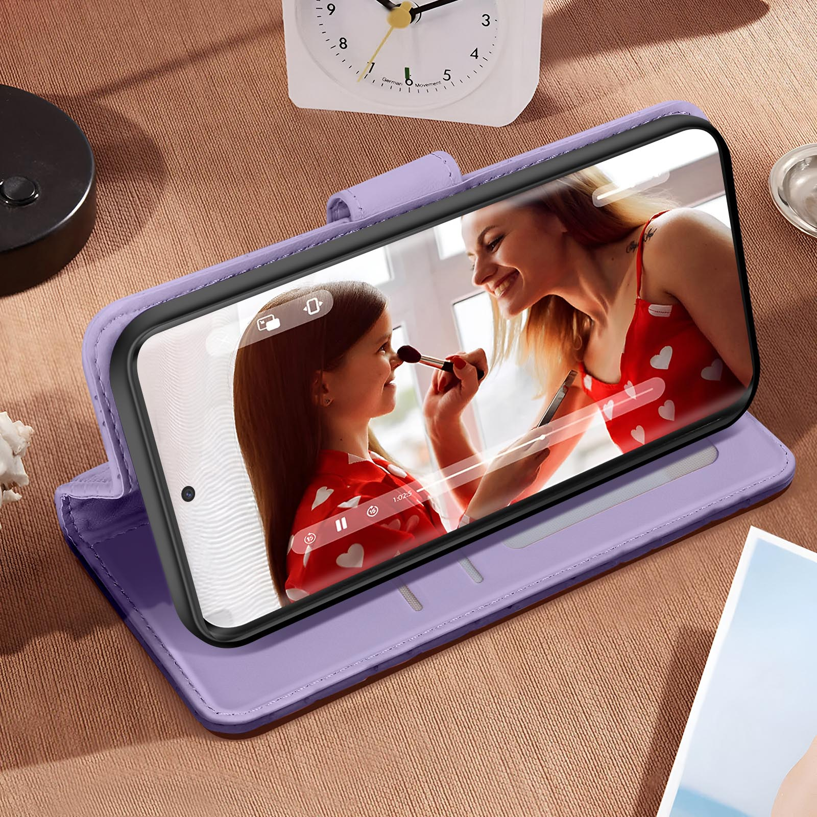 Custodia per telefono lilla con un telefono all'interno. Una donna applica il trucco a una ragazza sullo schermo.