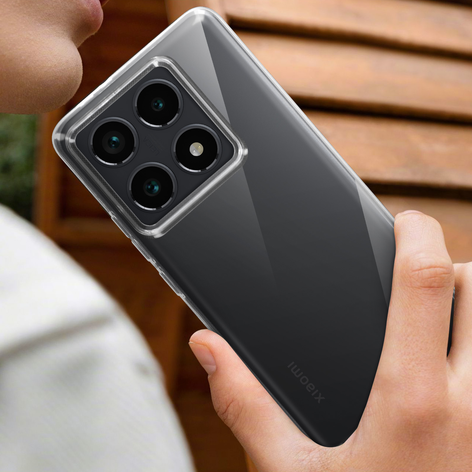 Una mano che tiene un telefono in una custodia trasparente. Il telefono ha quattro obiettivi e Xiaomi.