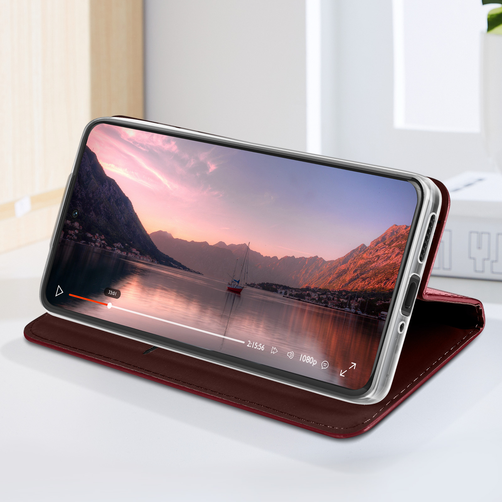 Téléphone dans étui bordeaux montrant une vidéo. Plage et montagnes dans la vidéo.