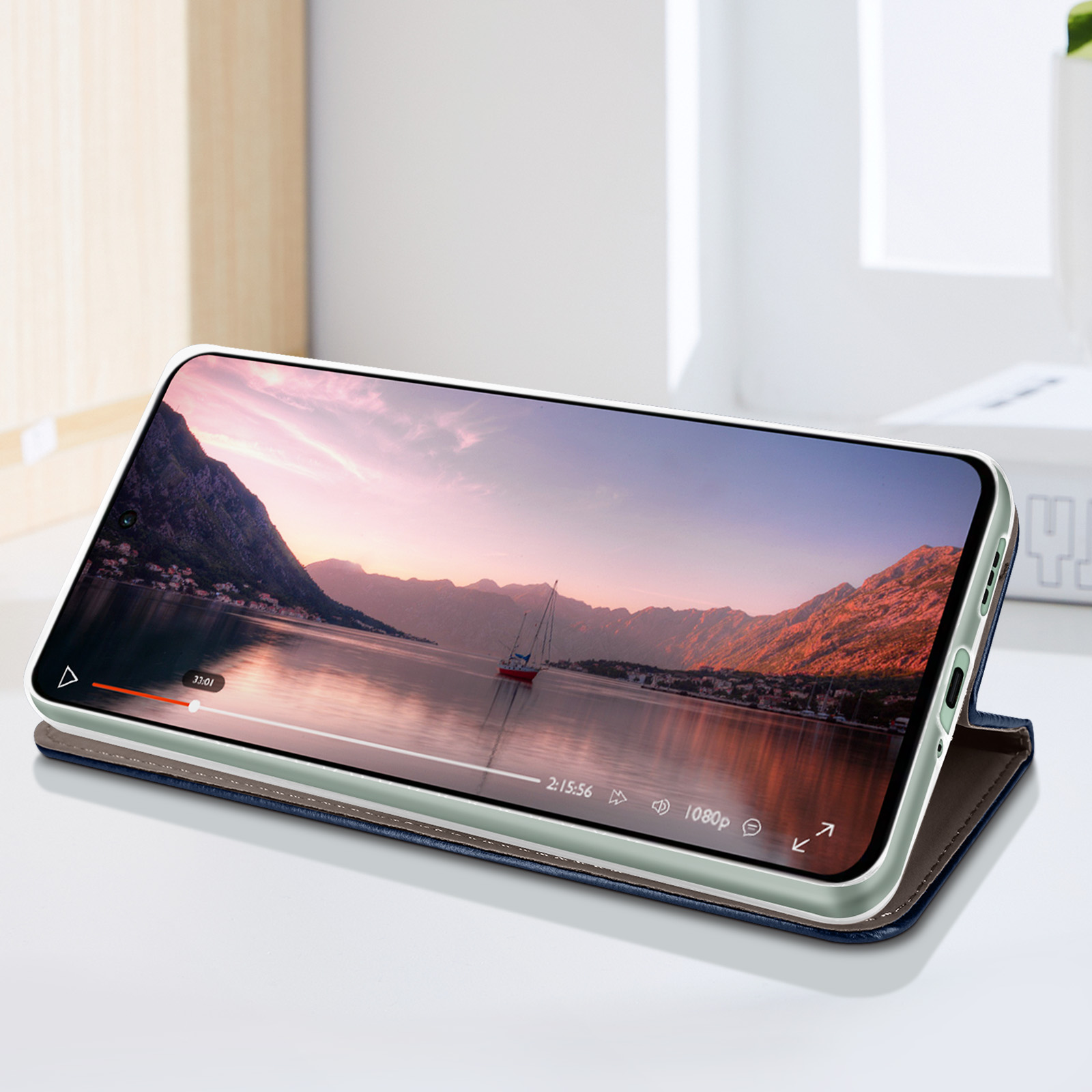 Telefono in custodia blu che mostra un video di un lago e montagne. Il telefono è su un tavolo.