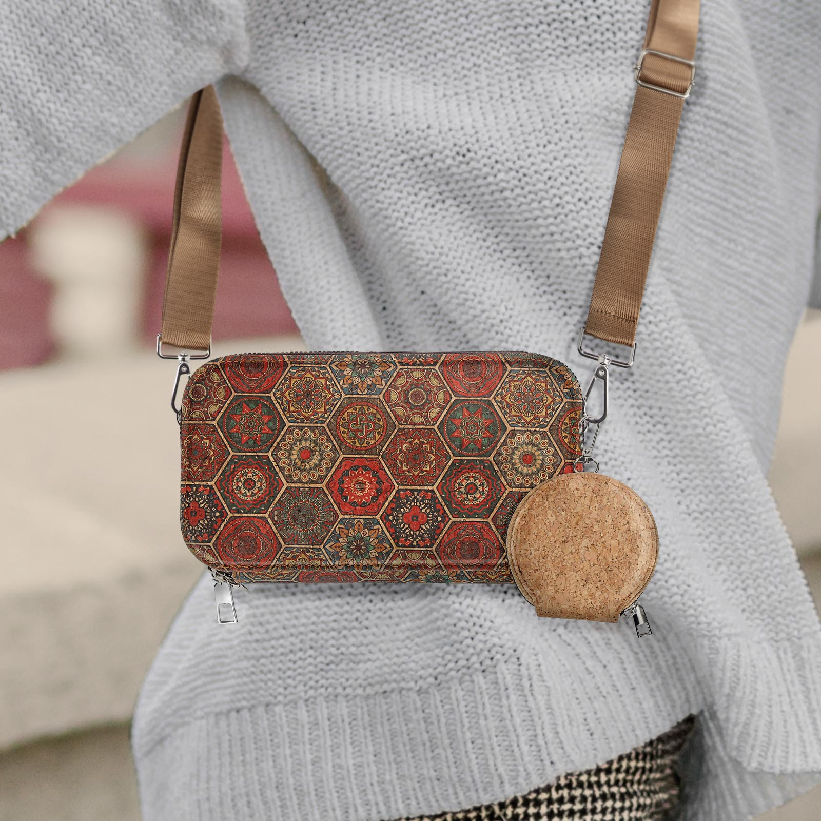 Person trägt einen weißen Pullover mit gemusterter Handtasche. Ein rundes Kork-Accessoire hängt.