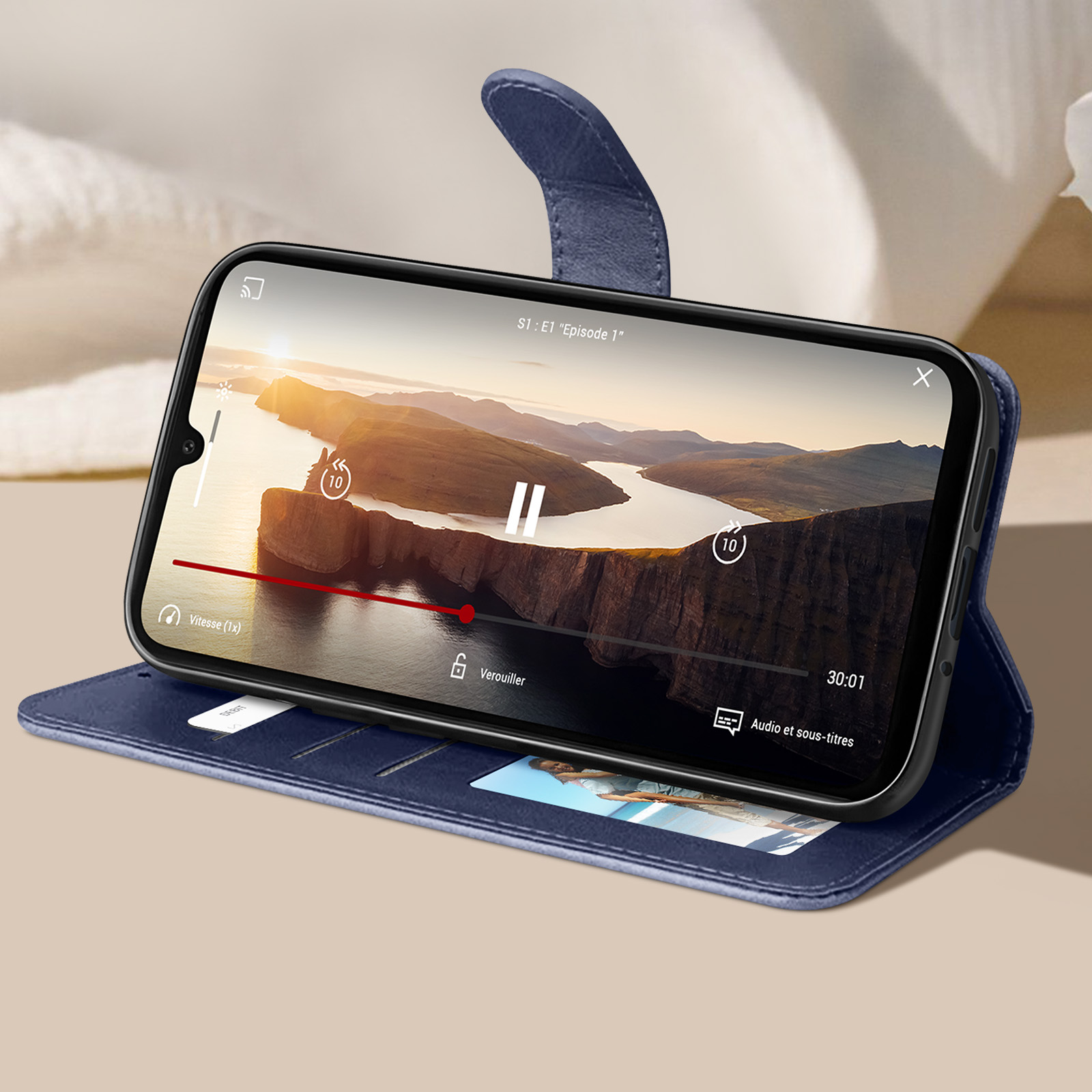 Telefono in custodia blu. Riproduzione video con icona di pausa sullo schermo. Custodia aperta, appoggiata su una superficie.