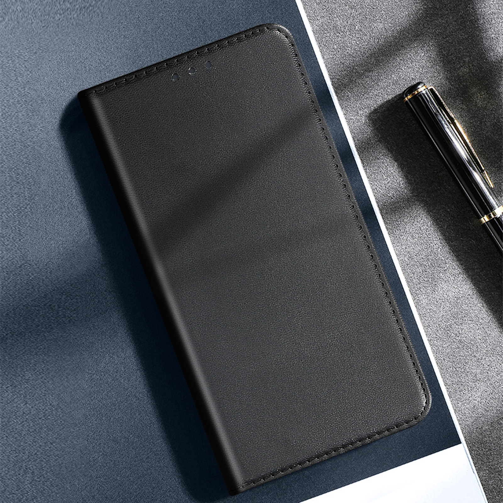 Custodia per telefono in pelle nera chiusa su una superficie blu, con una penna sullo sfondo.