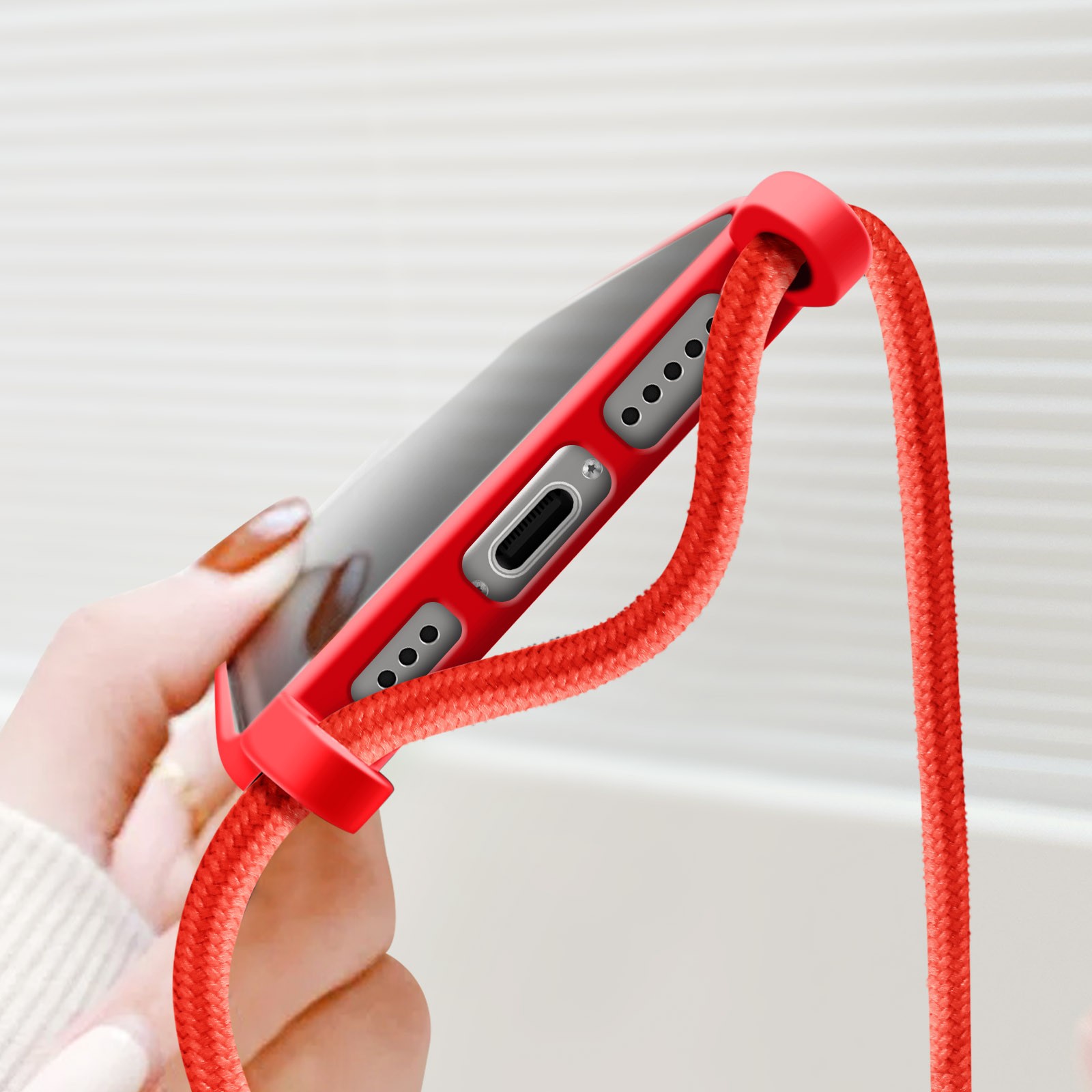 Una mano che tiene un telefono in una custodia rossa con un cordino rosso. Sfondo bianco.