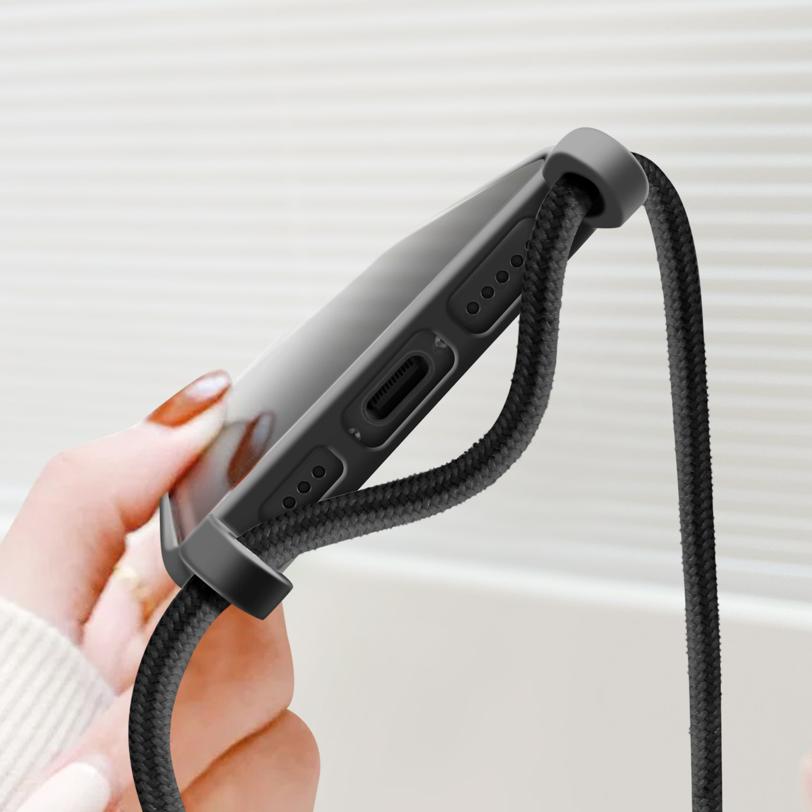 Mano che tiene un telefono in una custodia nera con un cordino nero. Sfondo bianco.