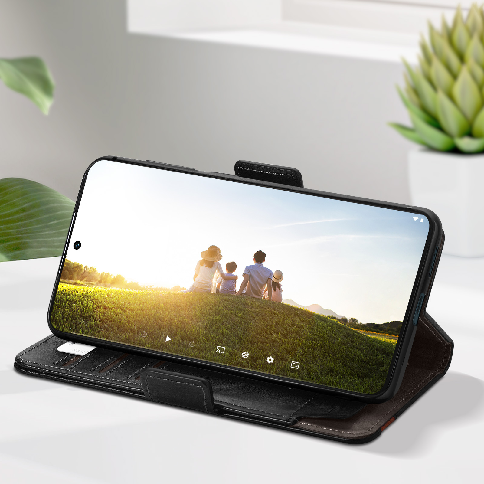 Telefono in custodia in pelle nera aperta. Lo schermo mostra una famiglia sull'erba.