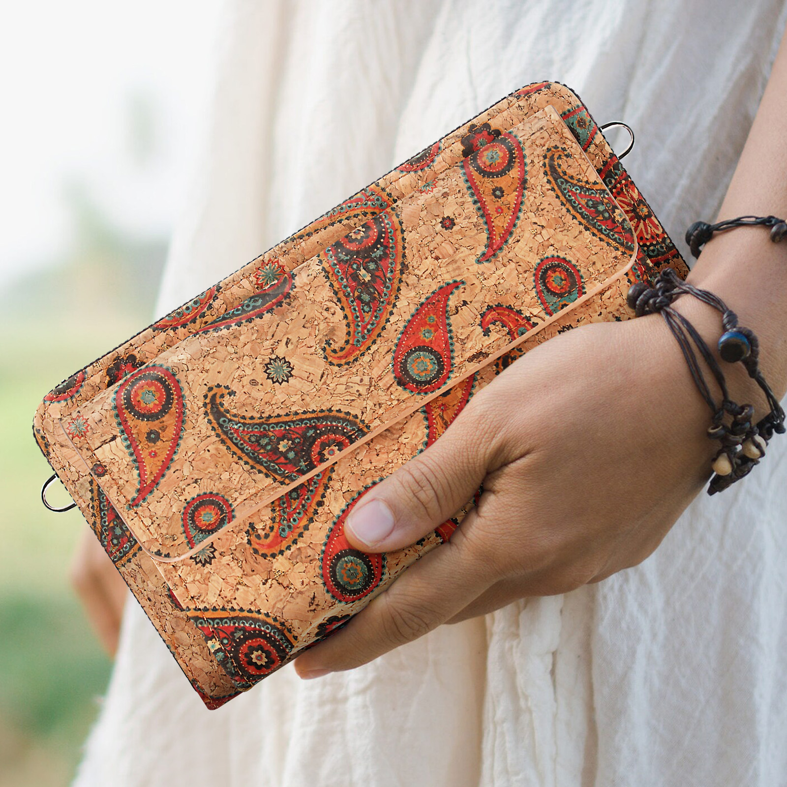 Eine Hand, die eine Korkbrieftasche mit farbenfrohem Paisley-Muster hält. Die Brieftasche hat einen Reißverschluss.