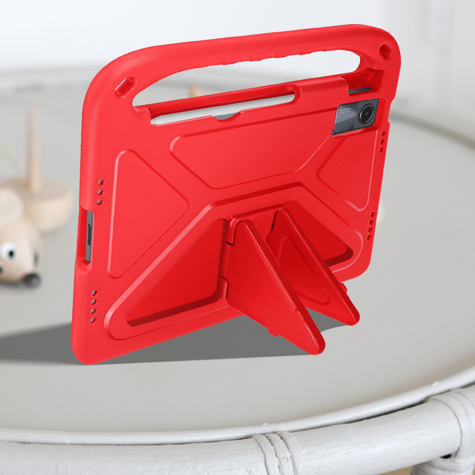 Custodia rossa per tablet con supporto, appoggiata su un tavolo bianco. Un giocattolo a forma di topo sfocato sullo sfondo.