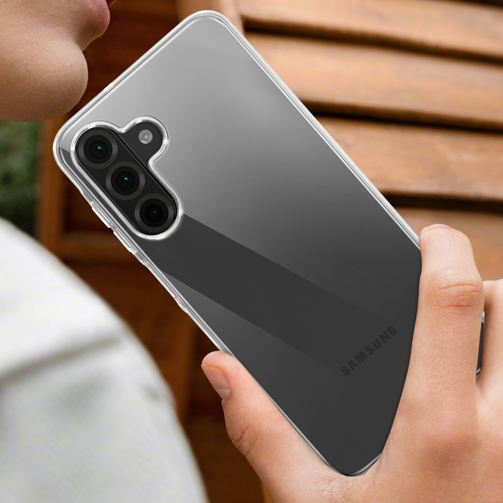 Una custodia trasparente per telefono tenuta da una persona. Il telefono ha una tripla fotocamera. Sfondo sfocato.