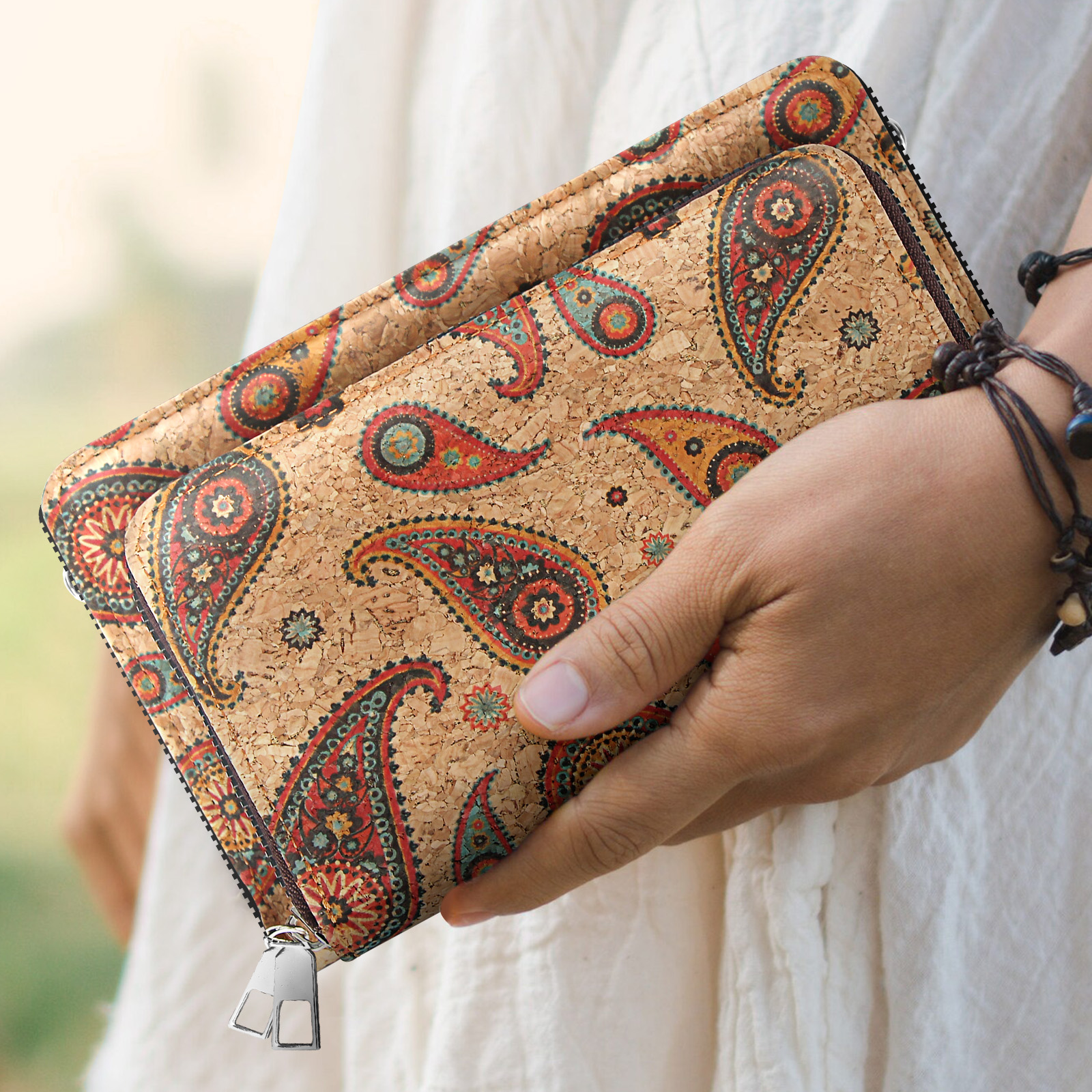 Hand hält eine Geldbörse mit Paisley-Muster. Sie hat einen braunen Reißverschluss und silberne Zipper.