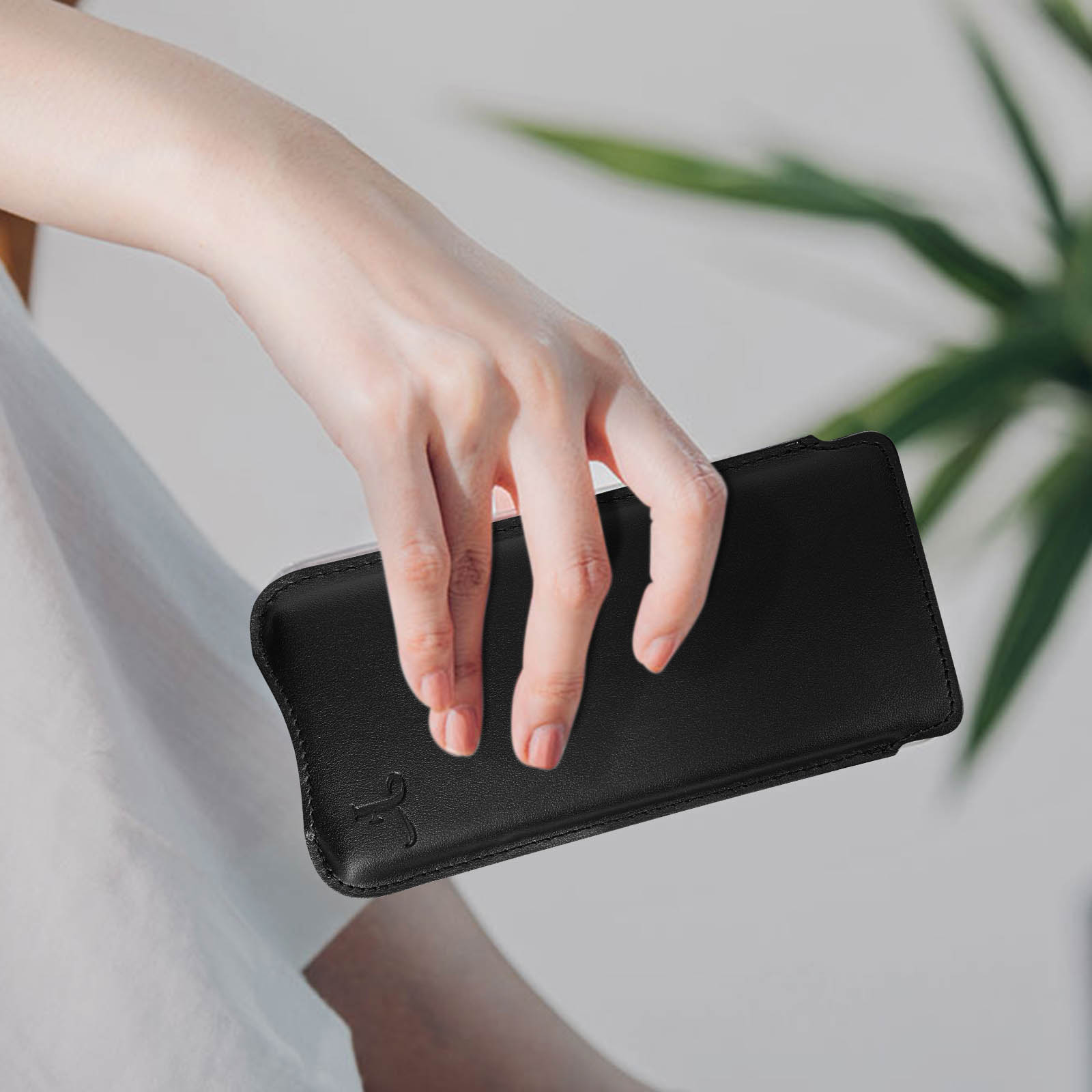 Mano che tiene una custodia per telefono in pelle nera, design semplice, sfondo bianco.