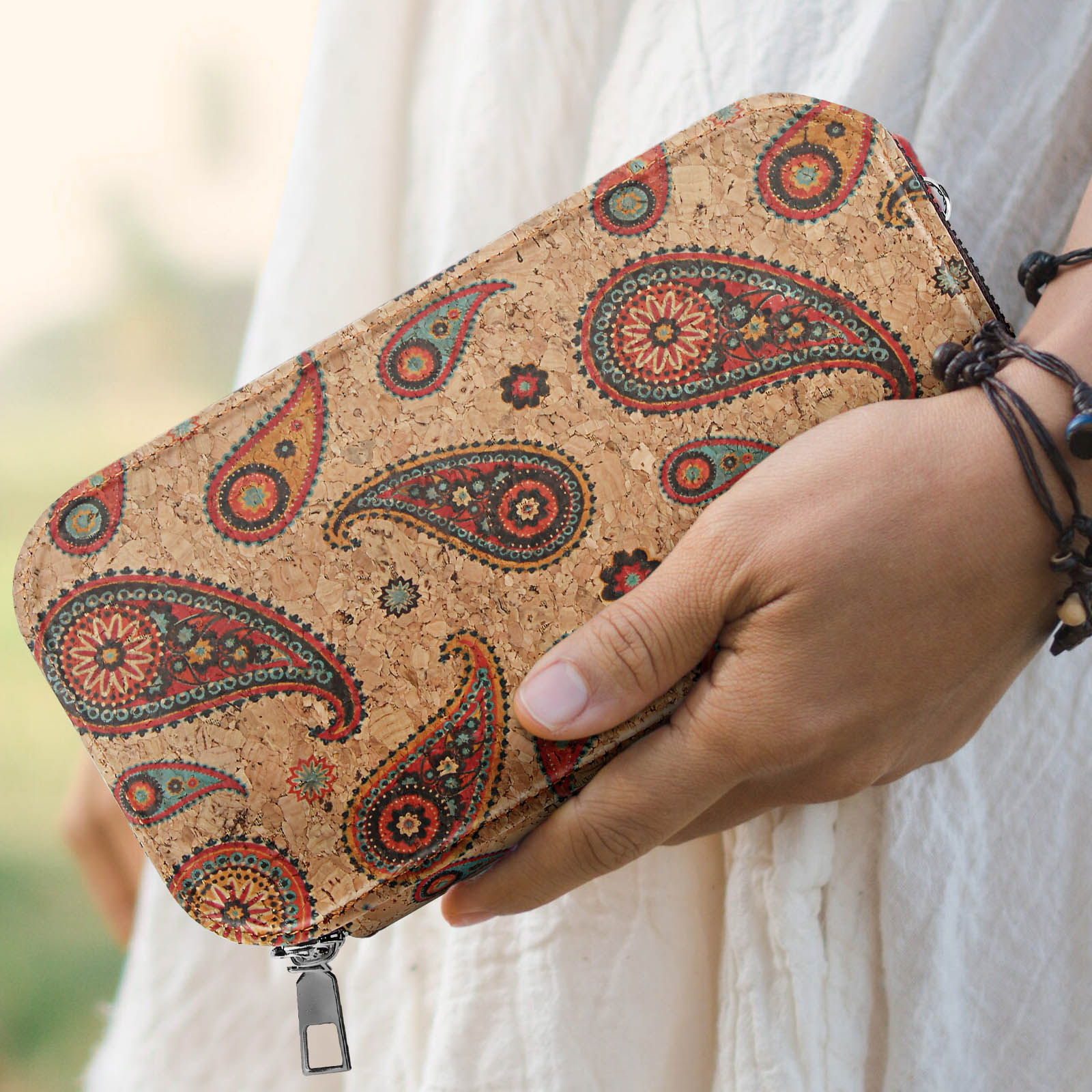 Person hält eine braune Korkbrieftasche. Es hat ein Paisley-Muster und einen Reißverschluss.
