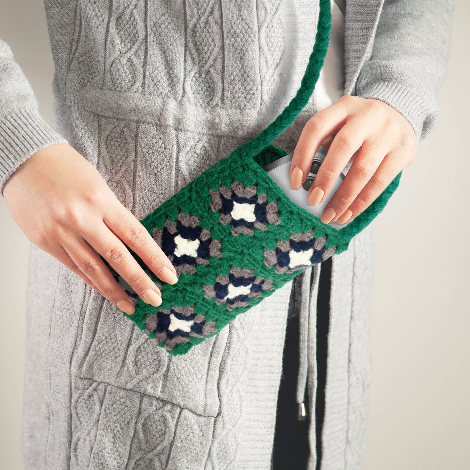 Una persona che tiene una borsa per telefono verde all'uncinetto con un telefono dentro.