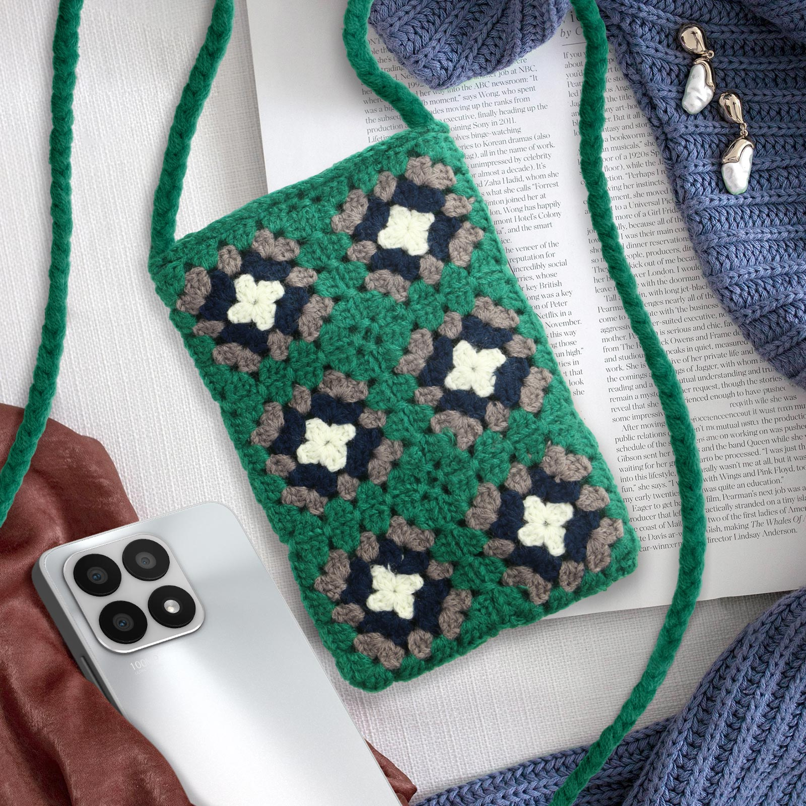 Borsa per telefono verde all'uncinetto con telefono all'interno, su maglione blu.