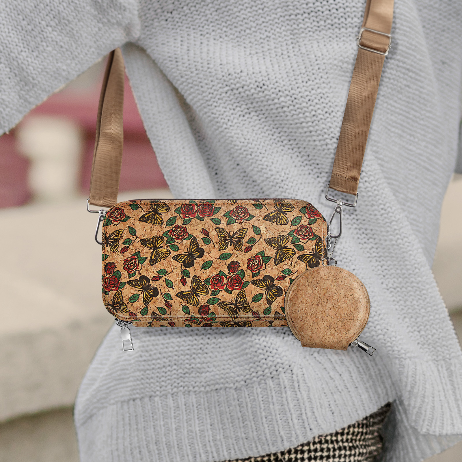 Frau trägt eine Tasche mit Schmetterlingen und Rosen. Passendes rundes Münzfach. Beiger Riemen und heller Pullover.