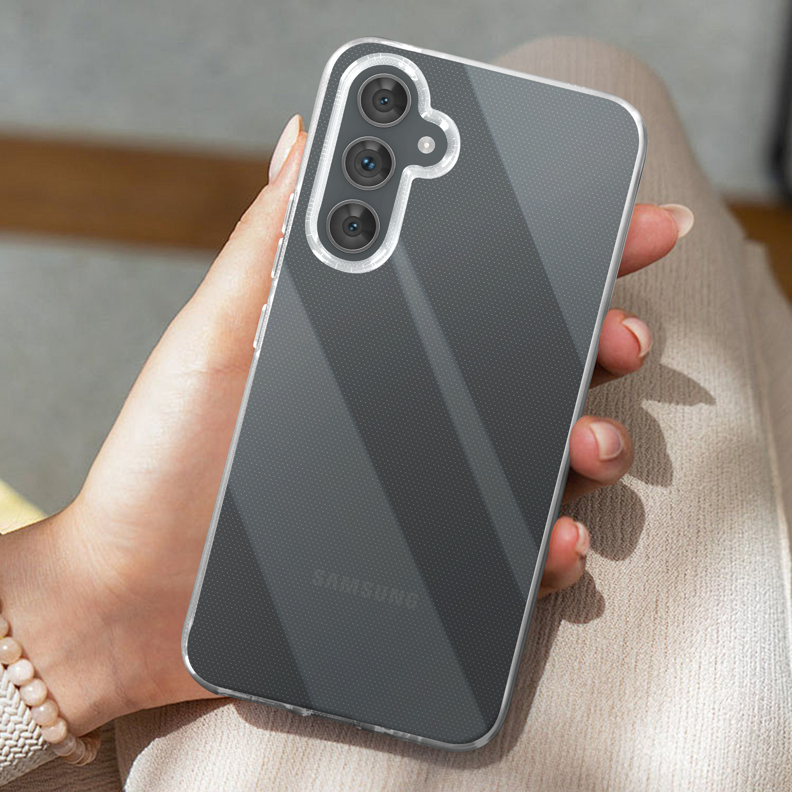 Una mano che tiene un telefono in una custodia trasparente, con sfondo sfocato.