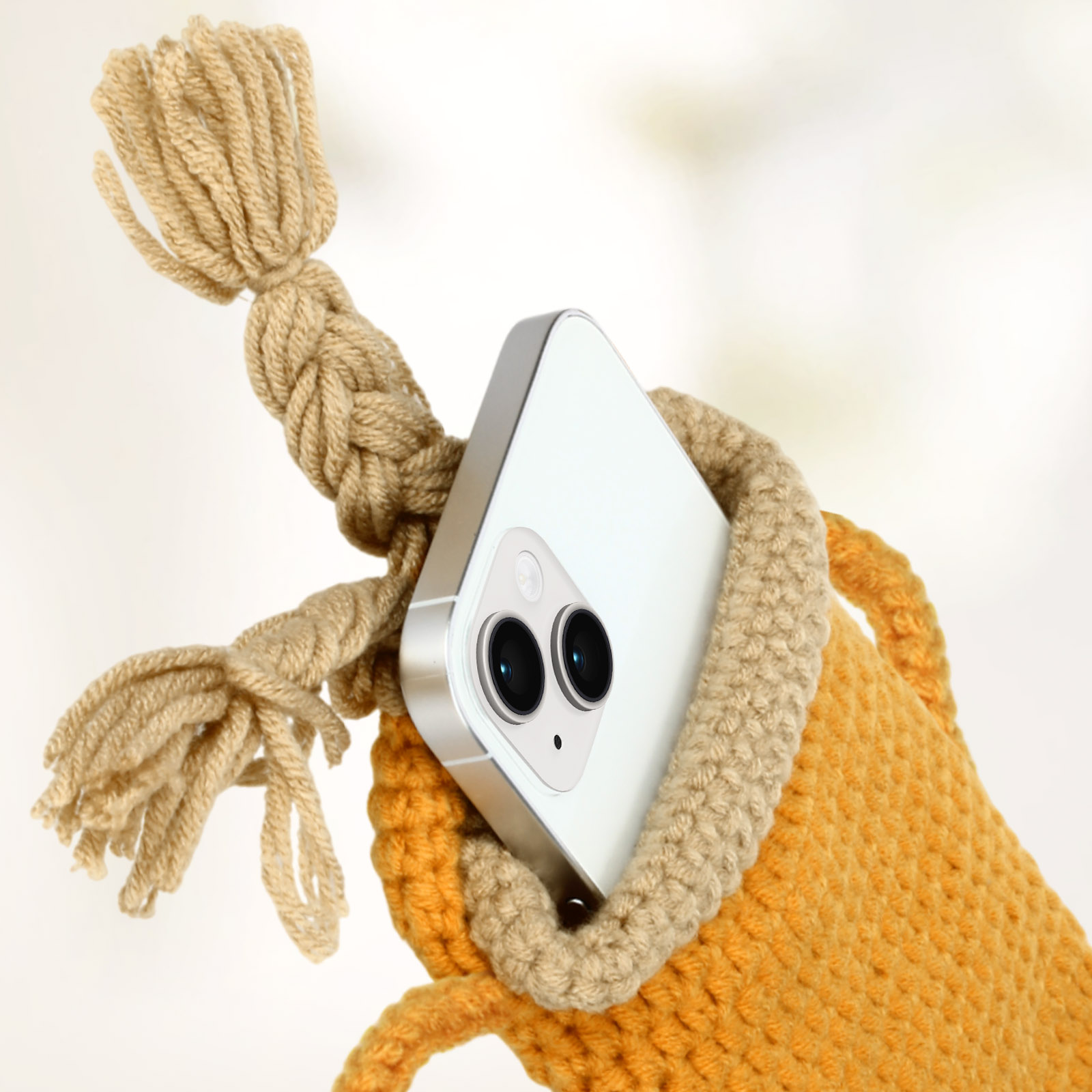 Un telefono bianco in una custodia arancione lavorata a maglia. La custodia ha una treccia.