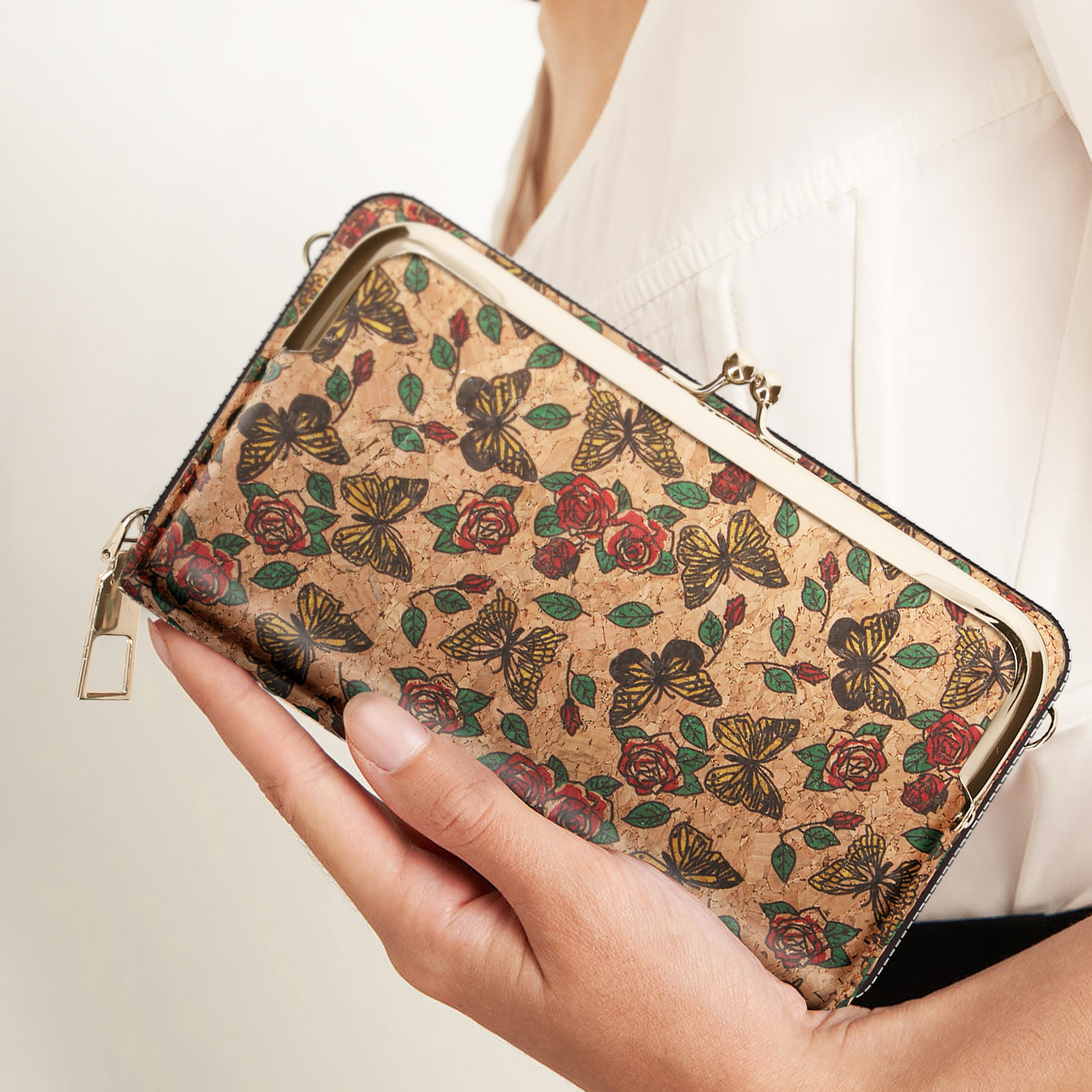 Eine Frau hält eine Kork-Clutch mit Schmetterlings- und Rosenmuster, Nahaufnahme, weißes Hemd.