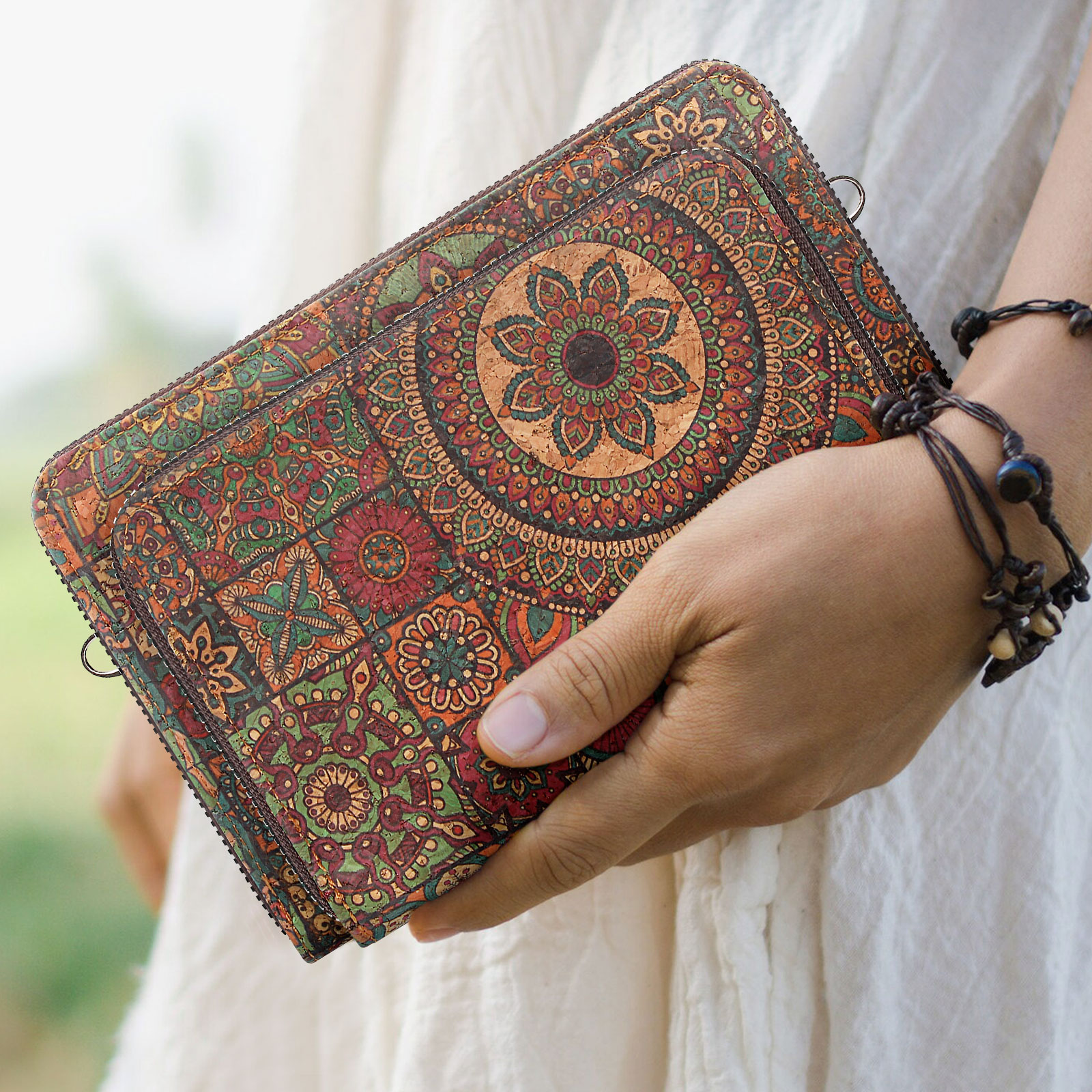 Frau hält eine Kork-Clutch mit Mandala-Muster. Weißes Hemd, verschwommener Hintergrund.