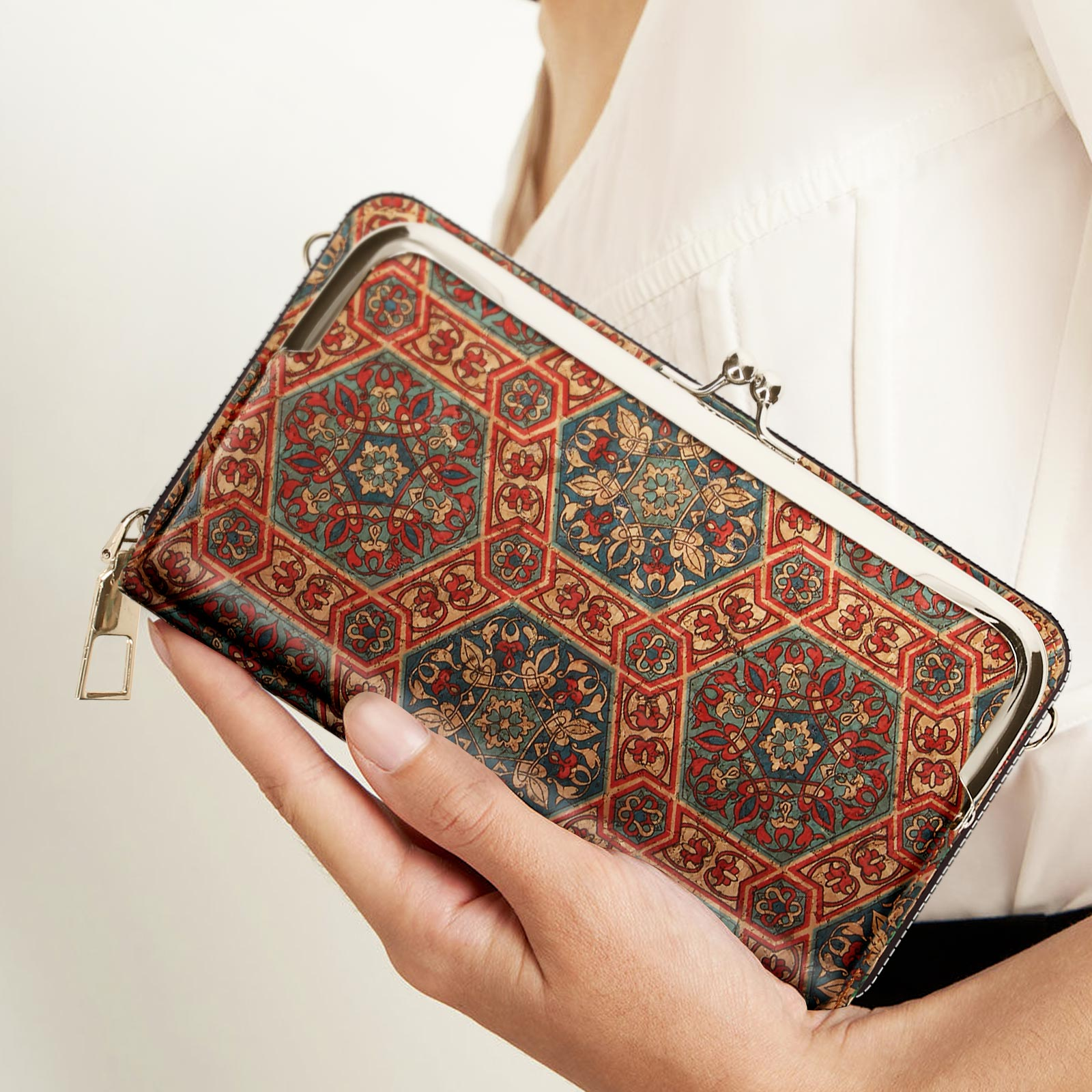 Hand hält eine gemusterte Telefonbrieftasche. Rote, blaue und beige Farben. Goldener Verschluss und Reißverschluss.