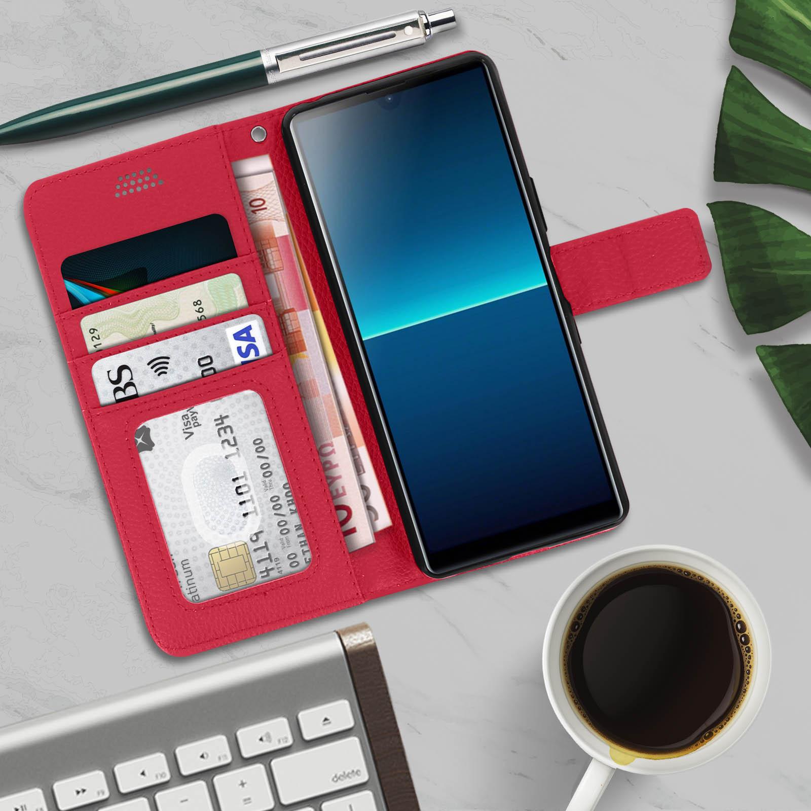 Custodia rossa aperta, con telefono, carte e denaro, con penna e caffè su superficie marmorea.