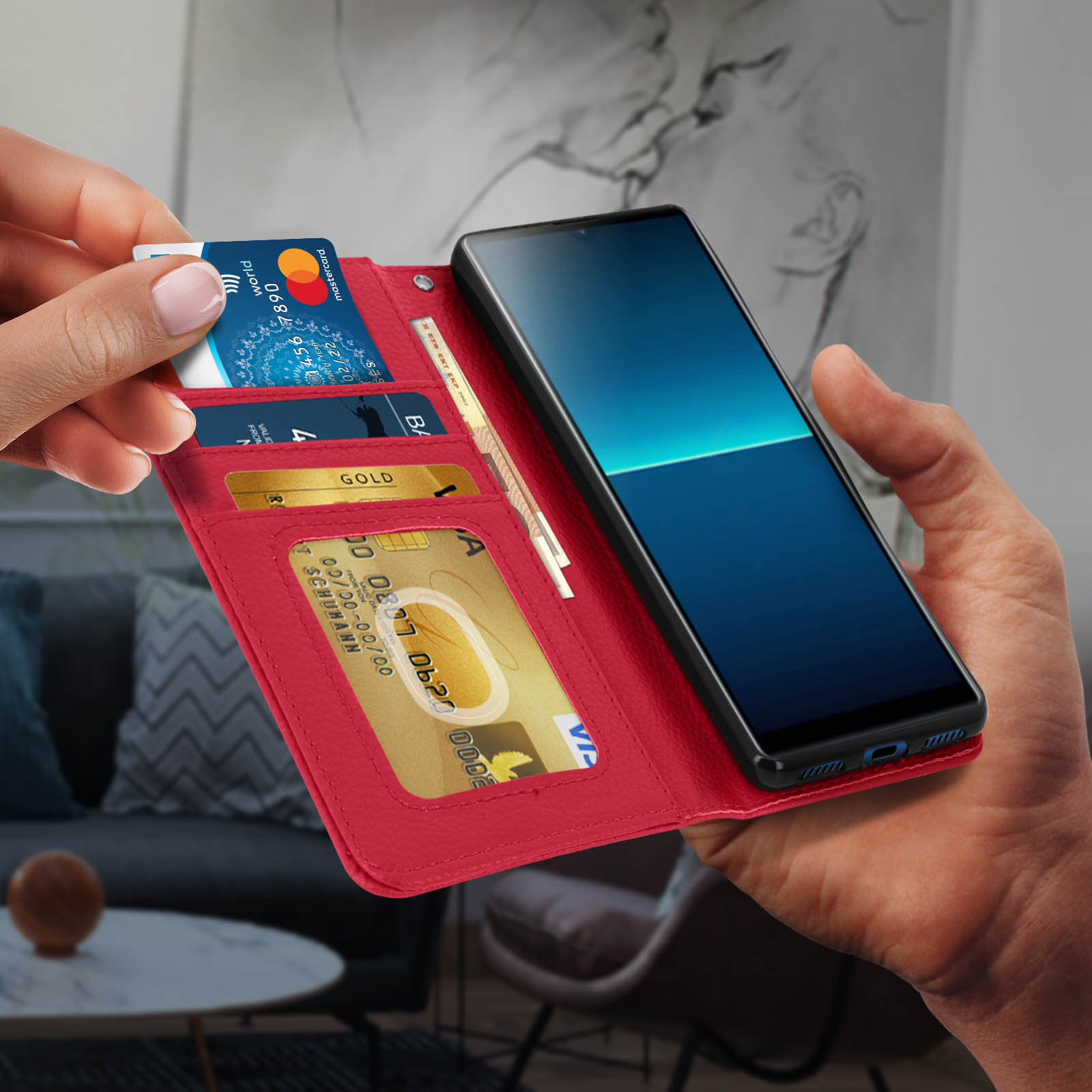 Mano che tiene aperta una custodia rossa, mostra carte di credito e telefono. Sfondo sfocato.