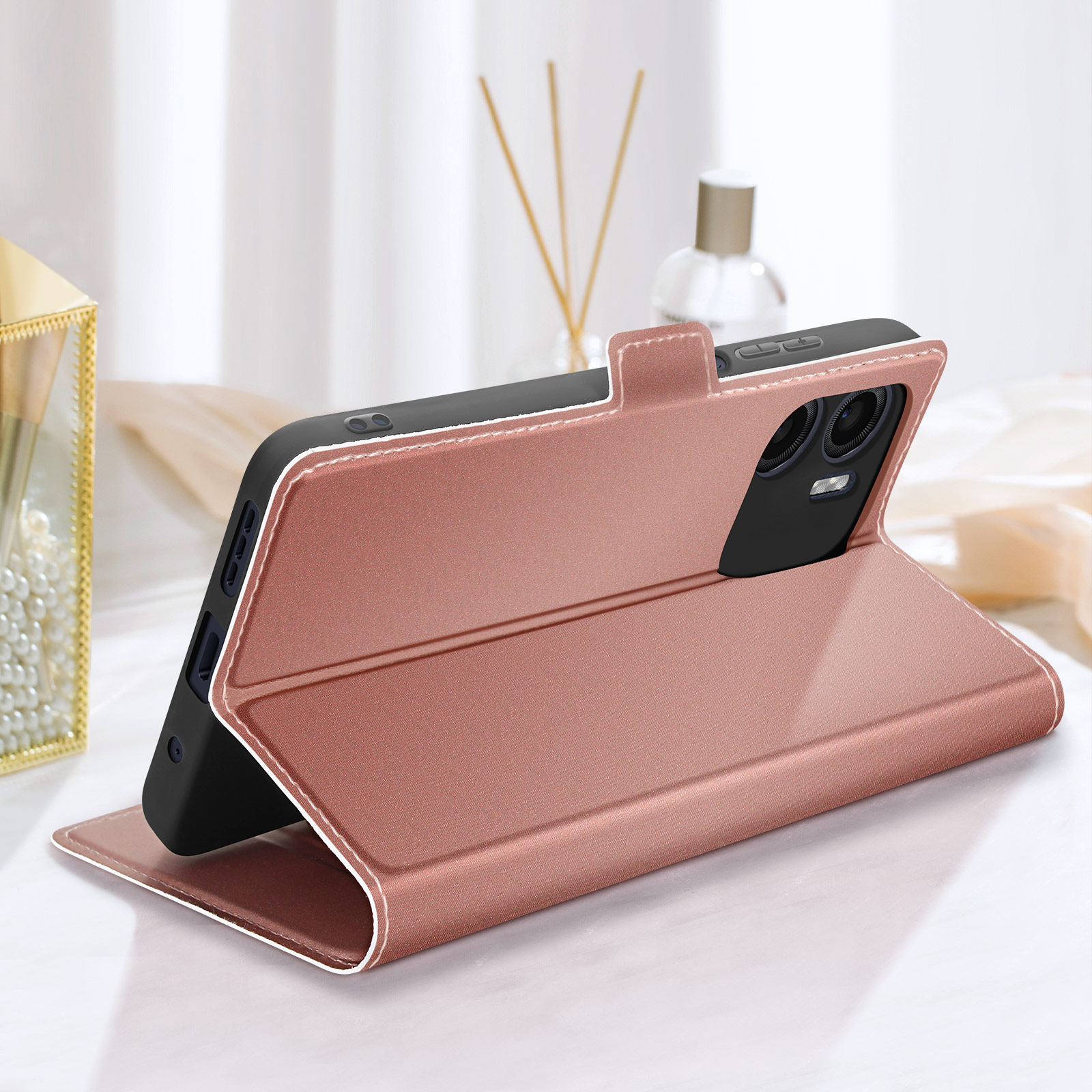 Custodia per telefono oro rosa, aperta. Un telefono è inserito. Lo sfondo include decorazioni e una bottiglia.