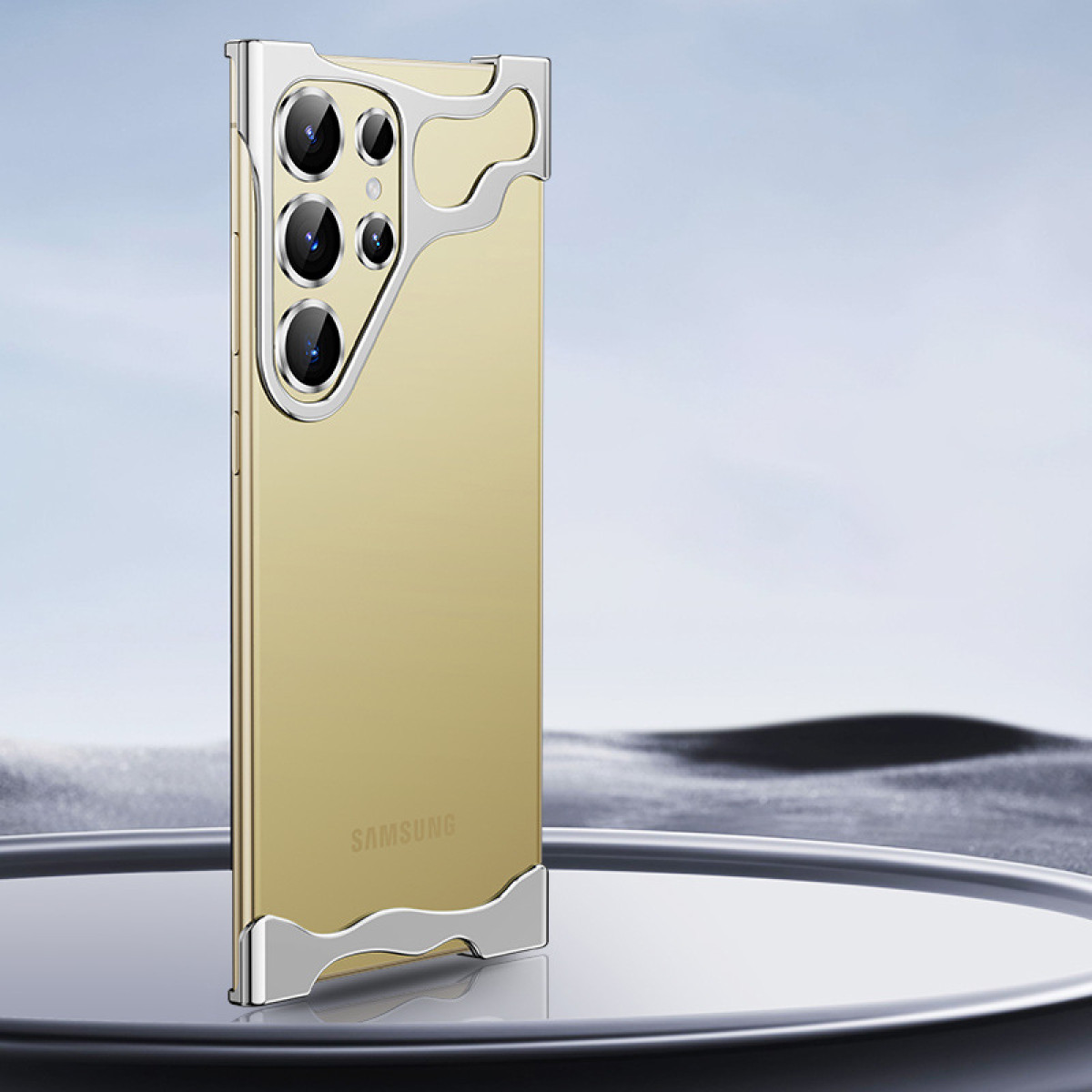Goldene Handyhülle mit einem Telefon darin. Silberne Einfassung an den Rändern. Die Hülle steht auf Glas.