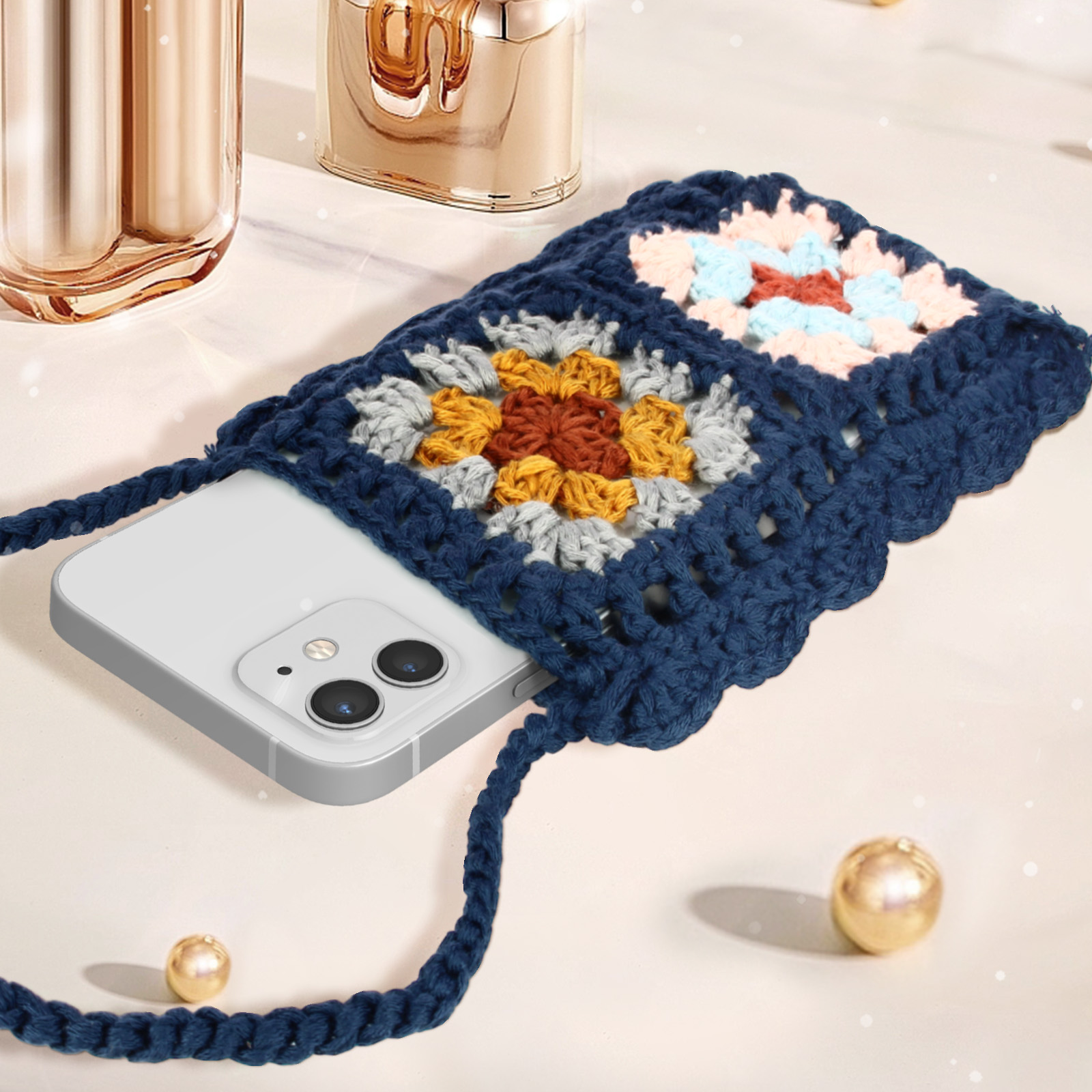 Una borsa a tracolla all'uncinetto blu navy con un telefono dentro, su un tavolo. Ci sono decorazioni.
