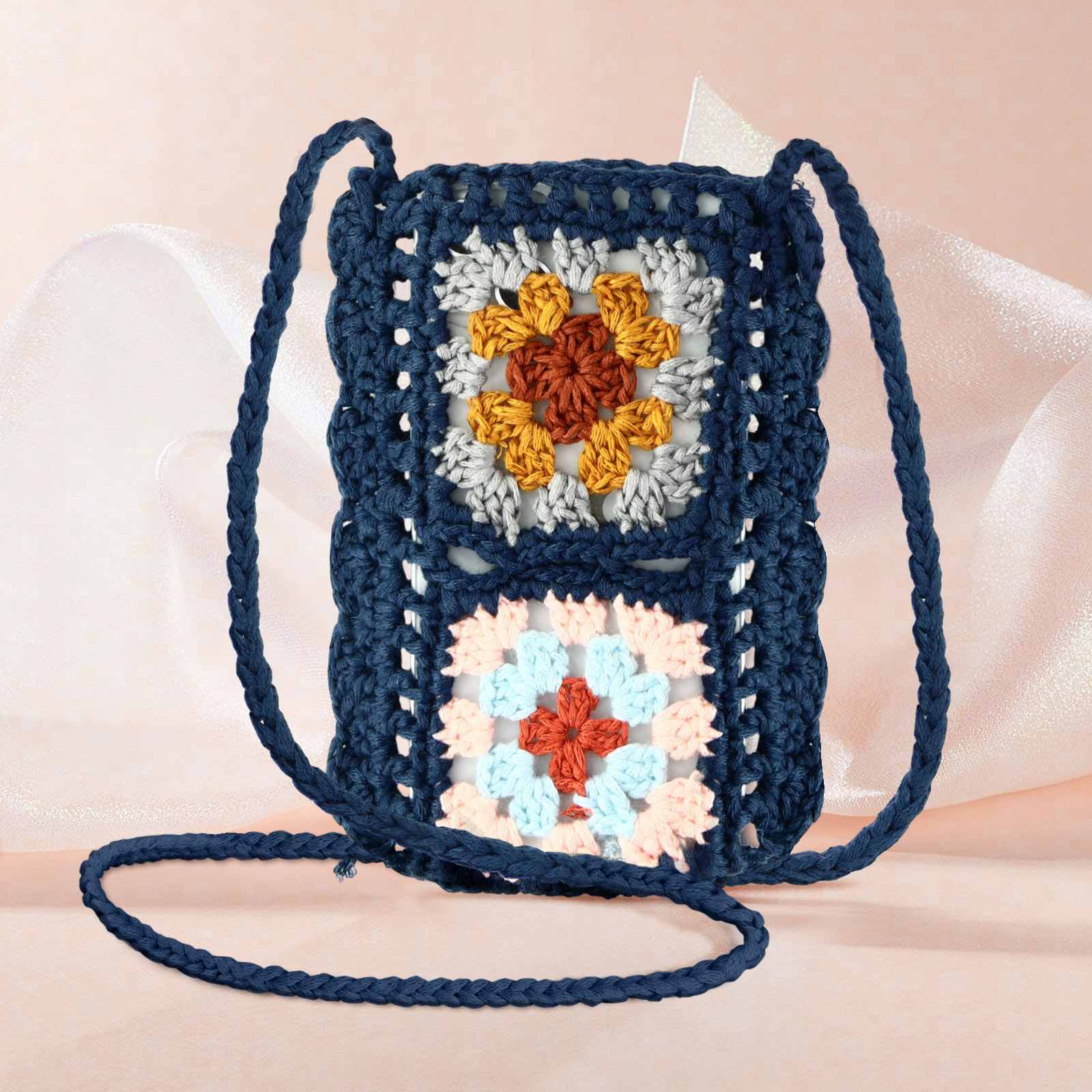 Borsa a tracolla all'uncinetto blu navy con quadrati floreali. La borsa è su sfondo rosa.